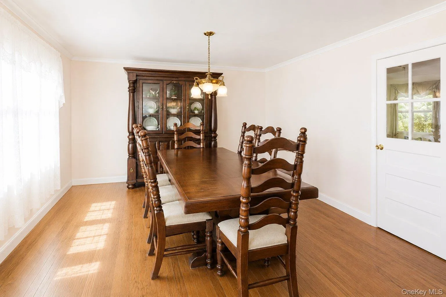 Wood-finish flooring anchors this room, complemented by a multi-pane glass door and a window with sheer coverings Wood-finish flooring anchors this room, complemented by a multi-pane glass door and a window with sheer coverings