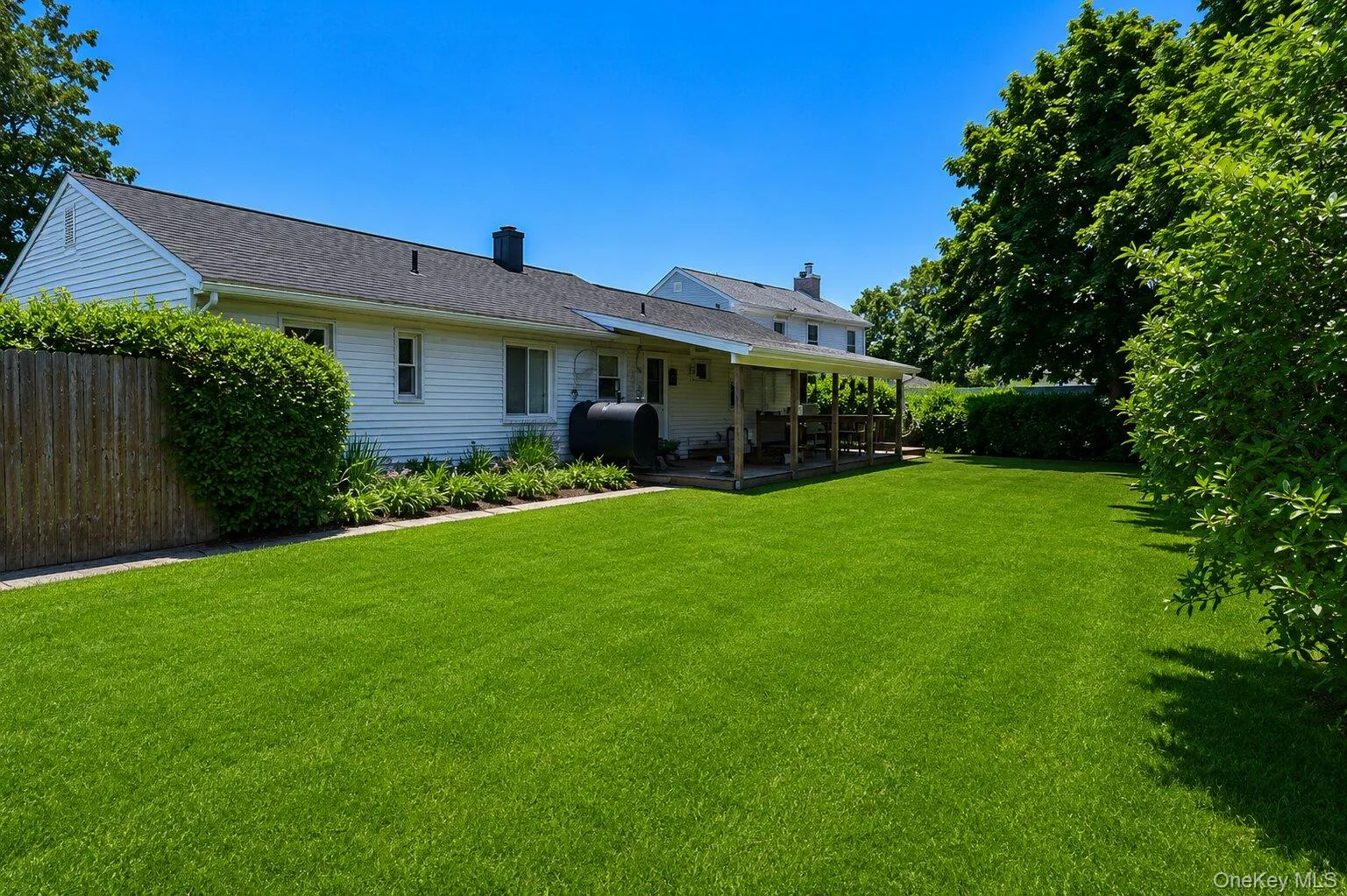 Expansive lawn with a covered deck, mature perimeter plantings, and a wooden privacy fence Expansive lawn with a covered deck, mature perimeter plantings, and a wooden privacy fence