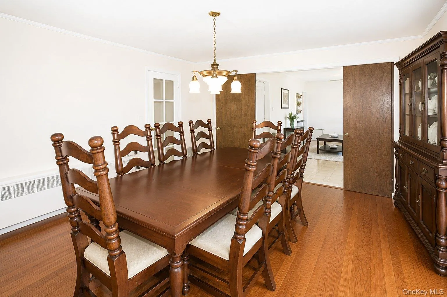 Hardwood flooring extends throughout this room, featuring a classic chandelier, crown molding, and a solid wood door frame Hardwood flooring extends throughout this room, featuring a classic chandelier, crown molding, and a solid wood door frame