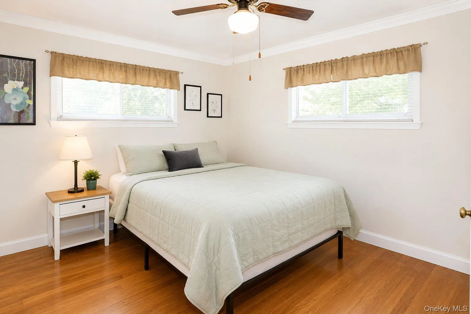 VIRTUALLY STAGED. Bright bedroom featuring wood-finish flooring, two windows, and a ceiling fan with integrated lighting VIRTUALLY STAGED. Bright bedroom featuring wood-finish flooring, two windows, and a ceiling fan with integrated lighting