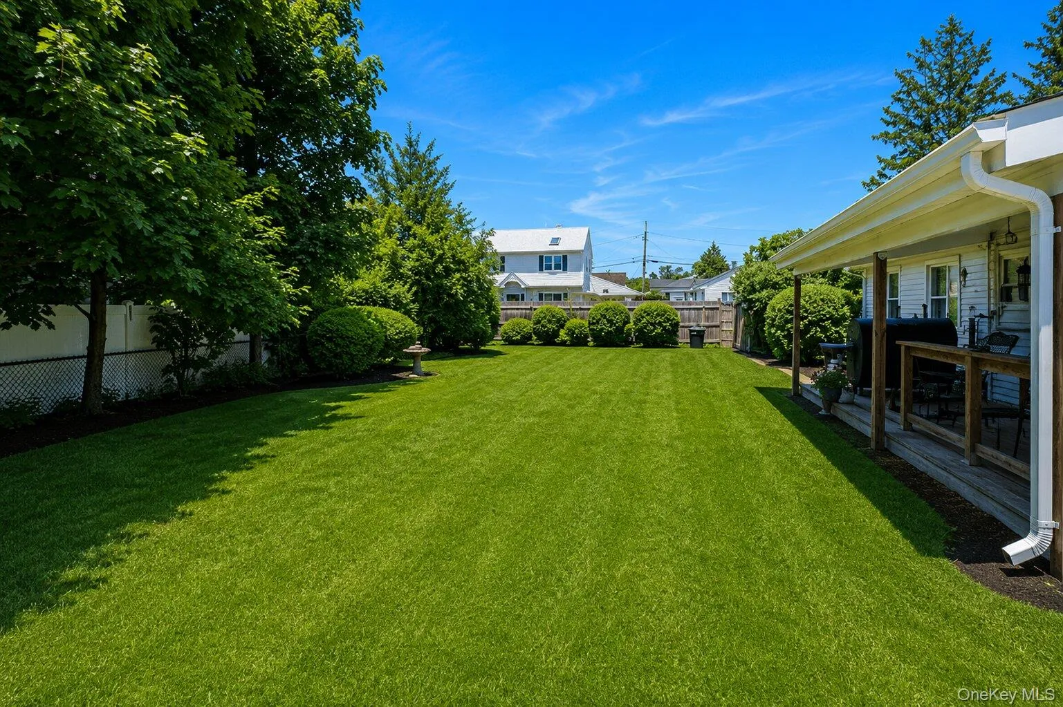 Expansive backyard featuring a lush lawn, mature trees, manicured shrubs, a privacy fence, and a covered porch with wood decking Expansive backyard featuring a lush lawn, mature trees, manicured shrubs, a privacy fence, and a covered porch with wood decking