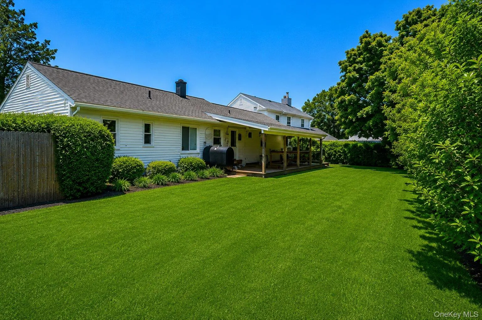 Expansive green lawn with a covered wood deck and mature perimeter landscaping Expansive green lawn with a covered wood deck and mature perimeter landscaping