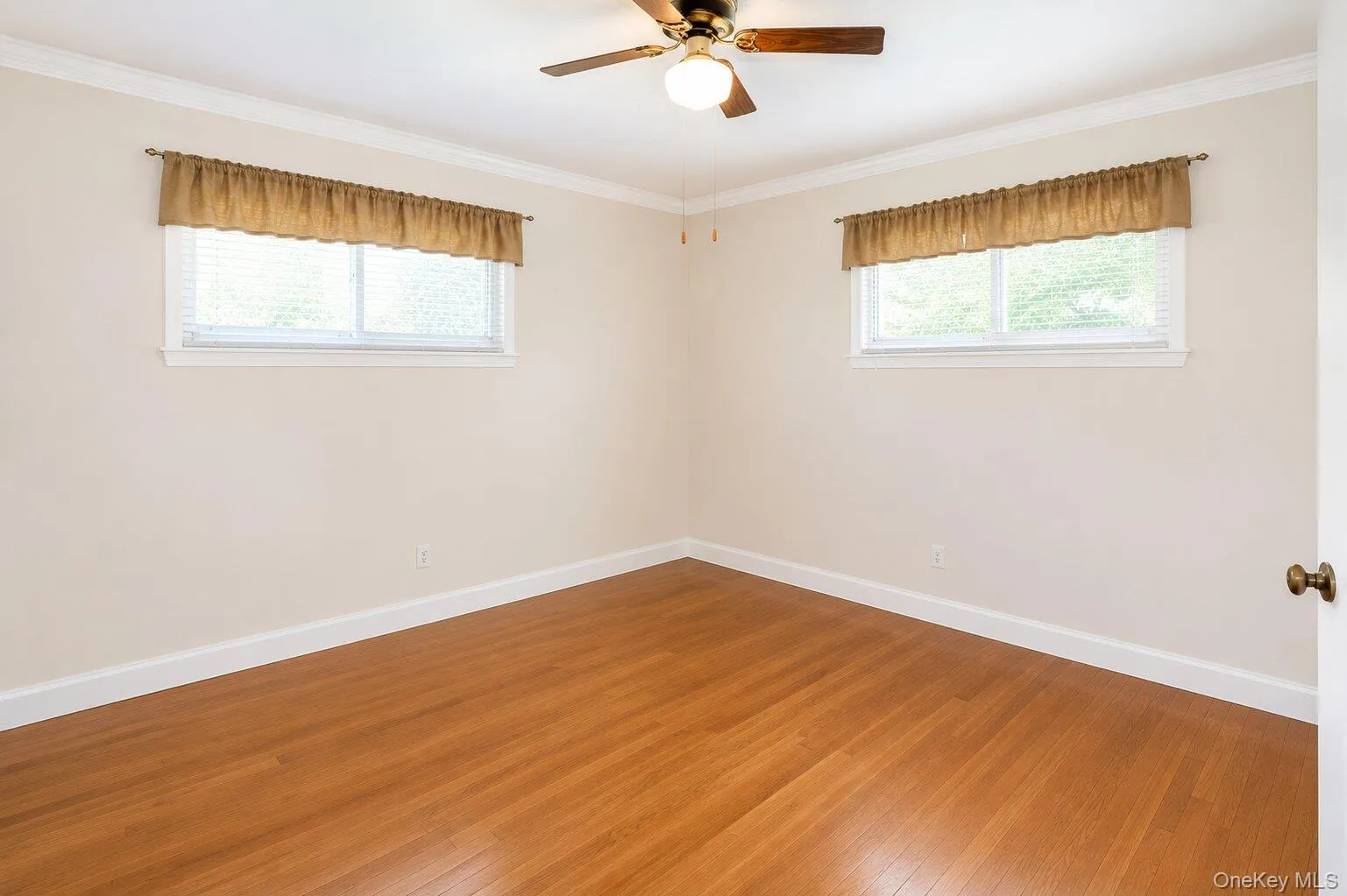 Room featuring wood-finish flooring, white baseboards, and white crown molding Room featuring wood-finish flooring, white baseboards, and white crown molding