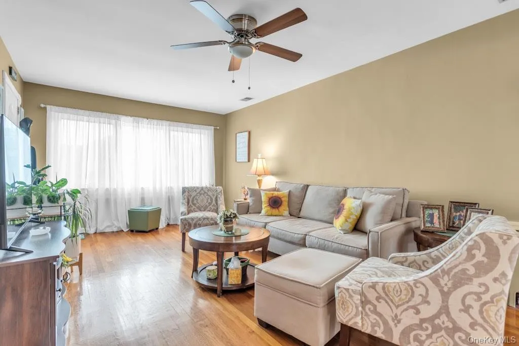 Living area featuring hardwood flooring, a ceiling fan, and a wide window with sheer coverings Living area featuring hardwood flooring, a ceiling fan, and a wide window with sheer coverings