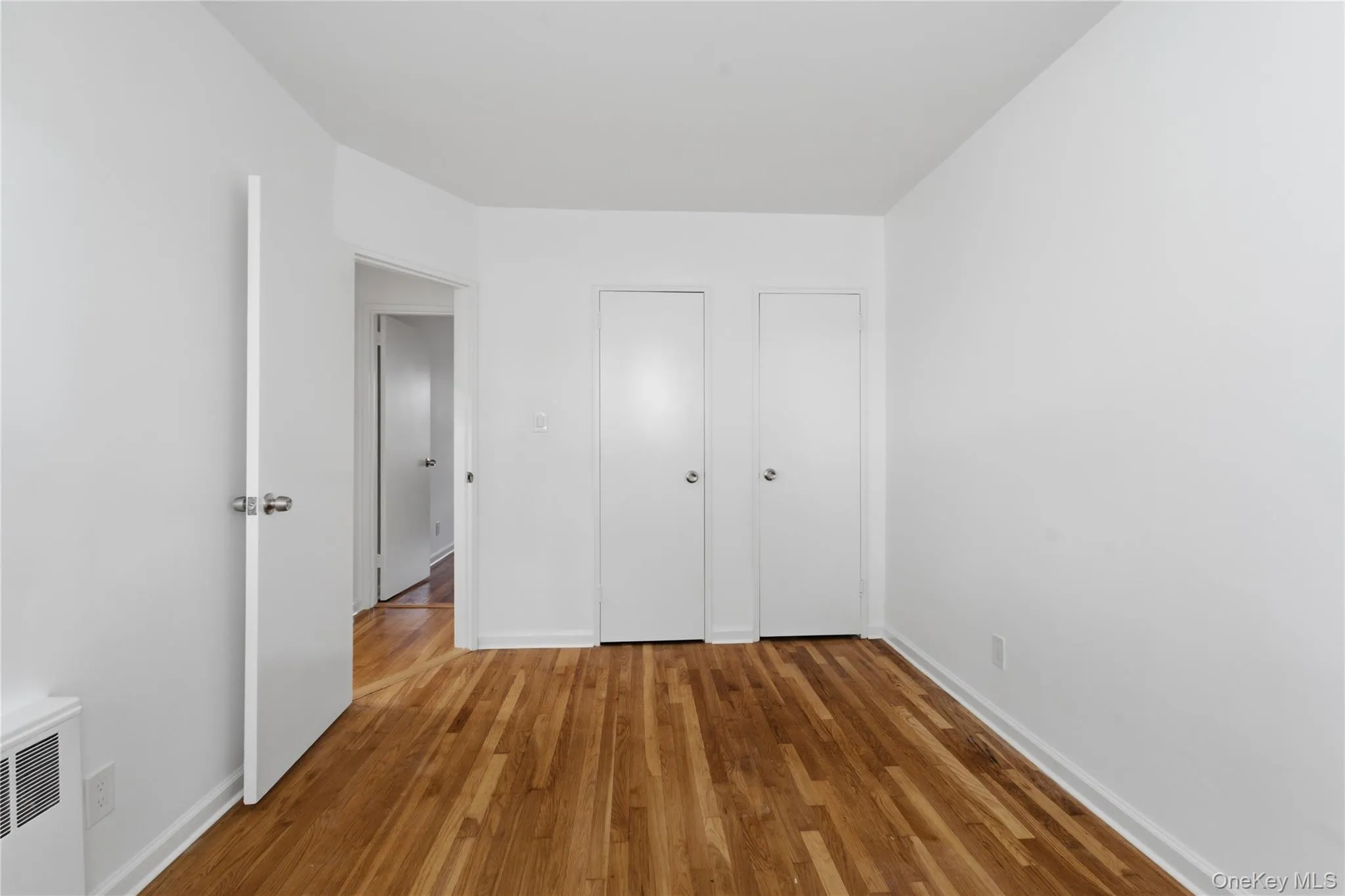Hardwood flooring throughout this room featuring a white door with polished chrome hardware and white baseboards Hardwood flooring throughout this room featuring a white door with polished chrome hardware and white baseboards