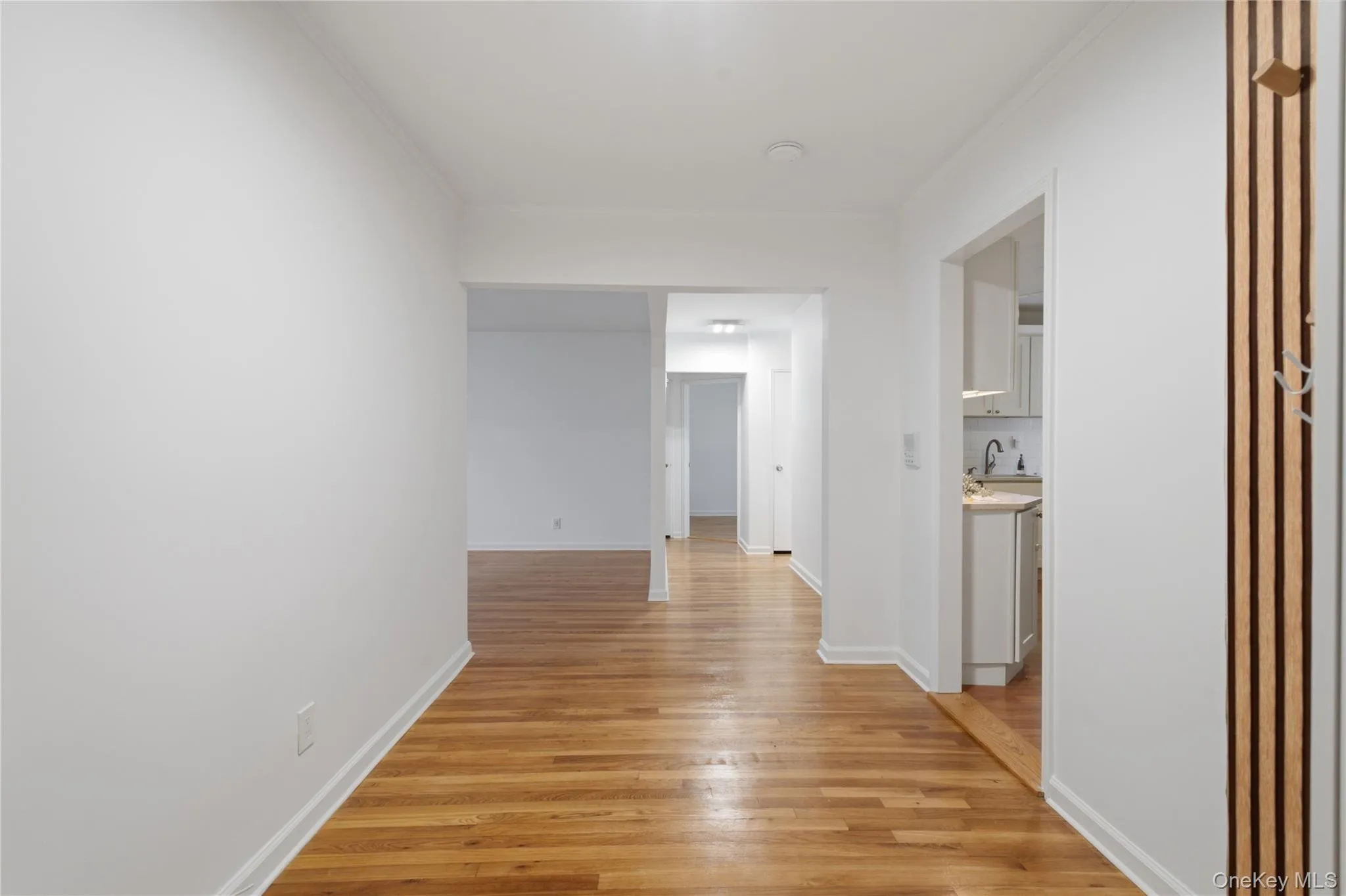Hardwood flooring extends throughout the hallway, complemented by white walls and ceiling Hardwood flooring extends throughout the hallway, complemented by white walls and ceiling
