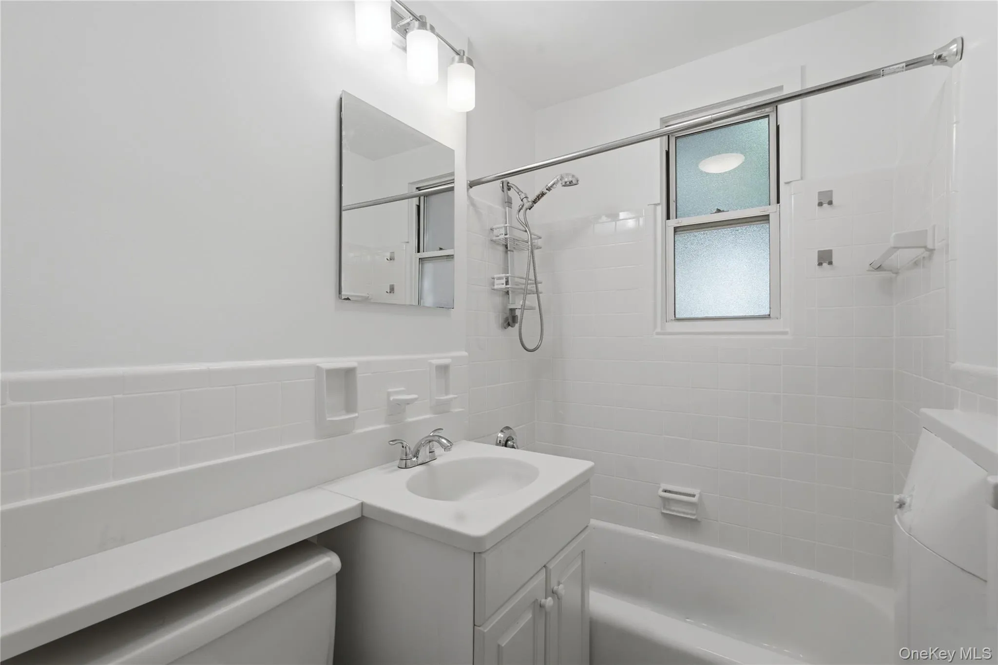 Bathroom featuring a white vanity with integrated sink, chrome faucet, wall-mounted mirror, and overhead light fixture Bathroom featuring a white vanity with integrated sink, chrome faucet, wall-mounted mirror, and overhead light fixture