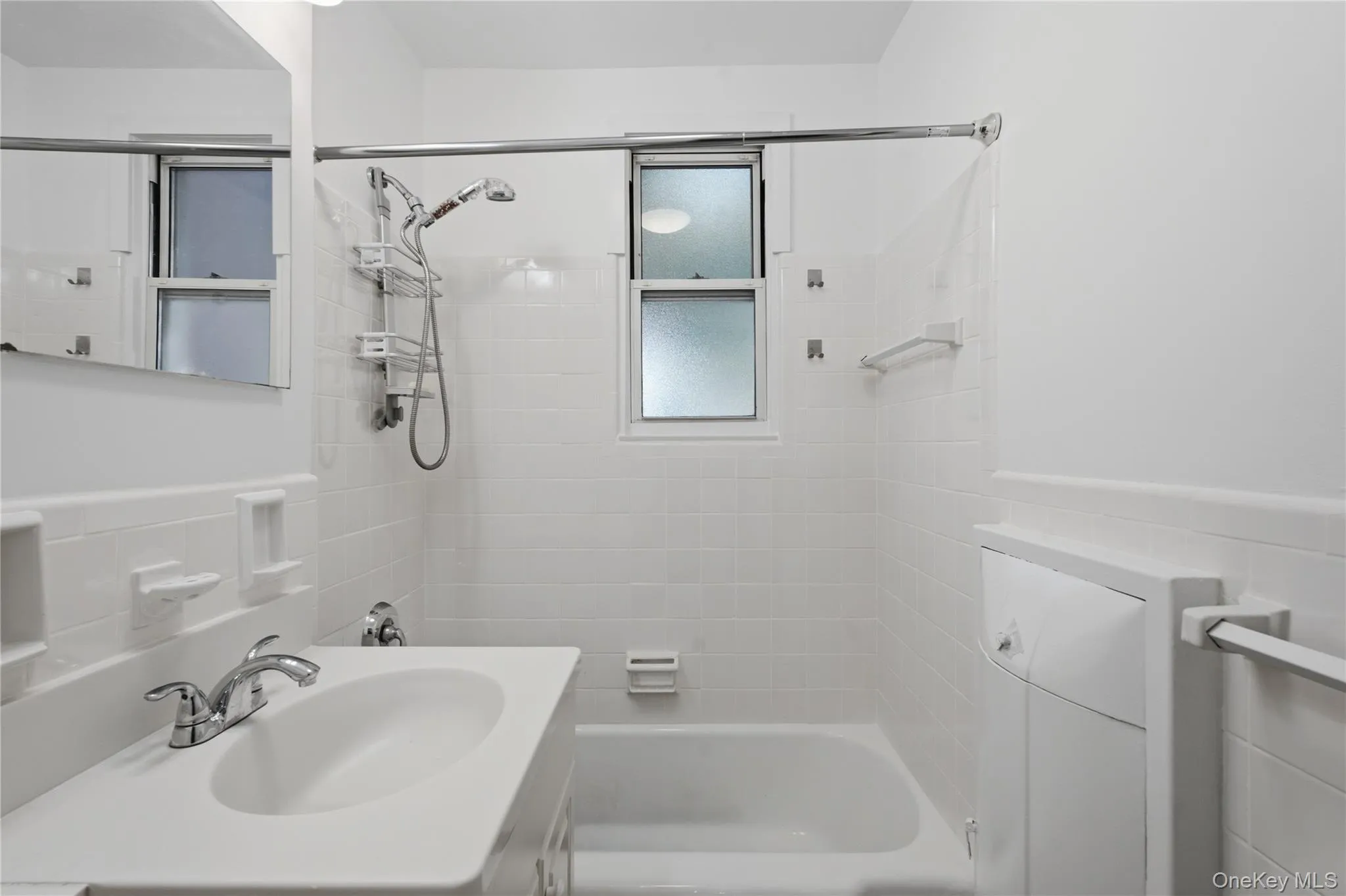 Bathroom with a white vanity sink, chrome faucet, and a shower-over-tub combination with white subway tile surround Bathroom with a white vanity sink, chrome faucet, and a shower-over-tub combination with white subway tile surround