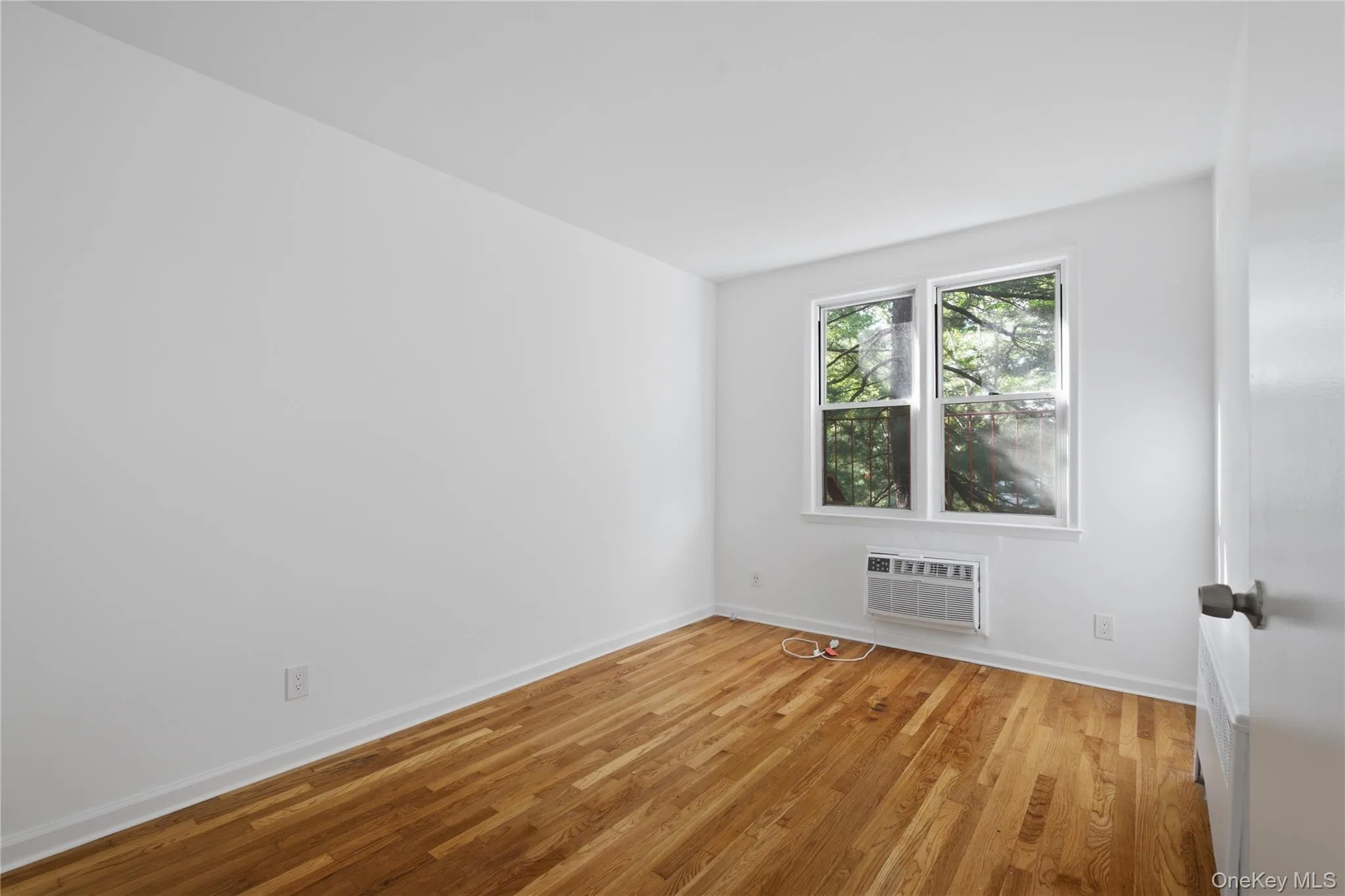 Hardwood flooring paired with a bright window, offering views of mature trees Hardwood flooring paired with a bright window, offering views of mature trees