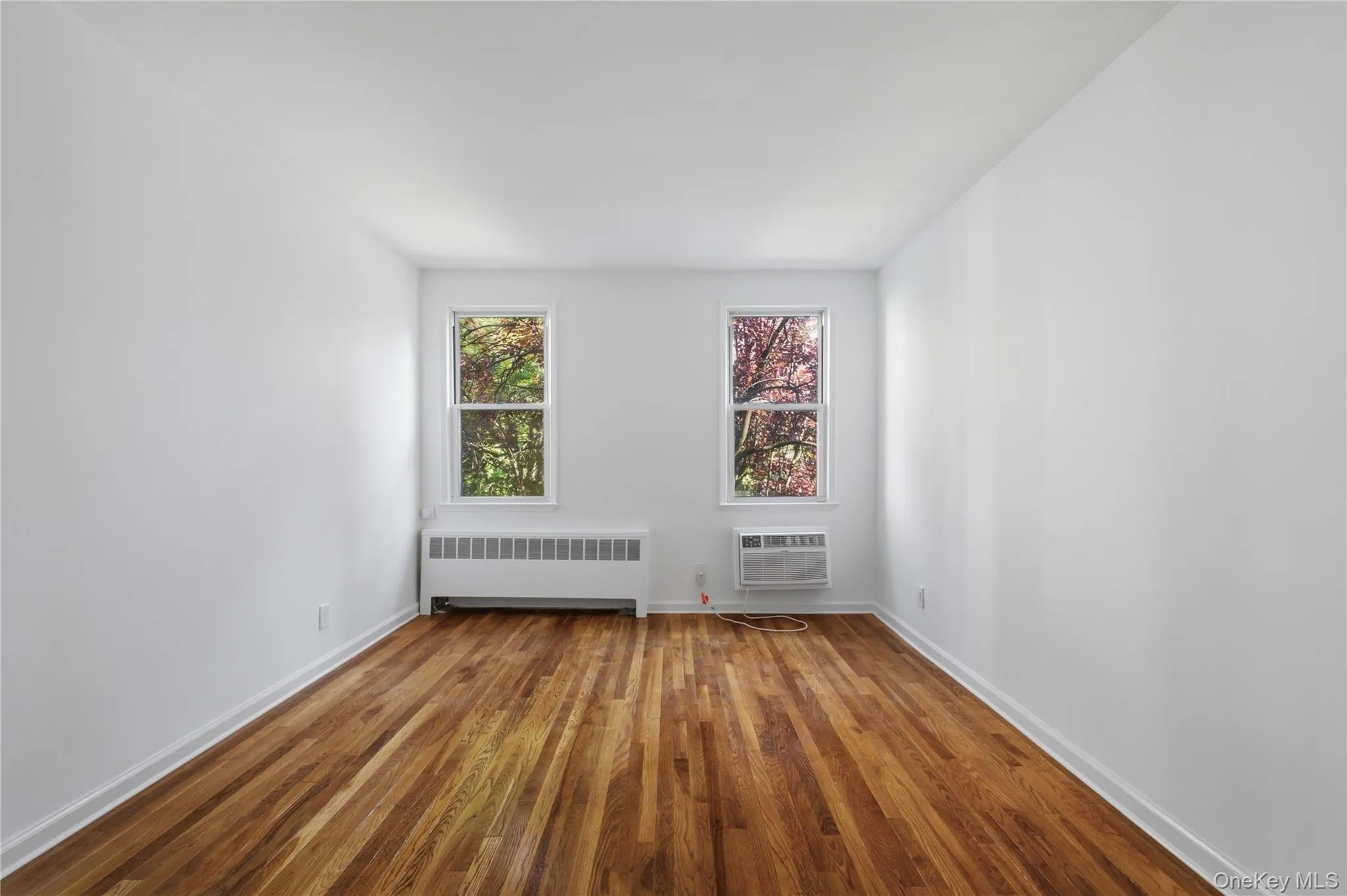 Hardwood flooring, white painted walls, two windows, window-mounted air conditioning unit, and a baseboard heating unit Hardwood flooring, white painted walls, two windows, window-mounted air conditioning unit, and a baseboard heating unit