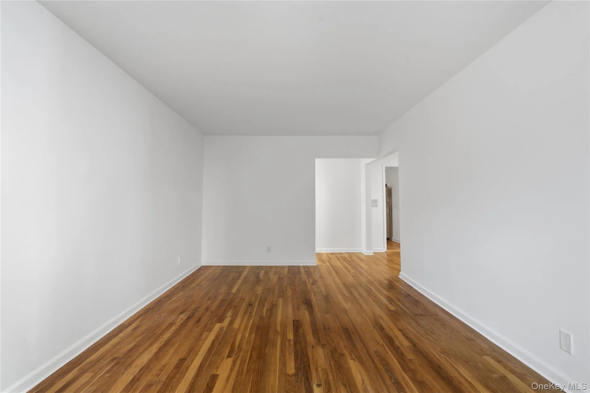 Hardwood flooring throughout a spacious room with white walls and baseboards Hardwood flooring throughout a spacious room with white walls and baseboards