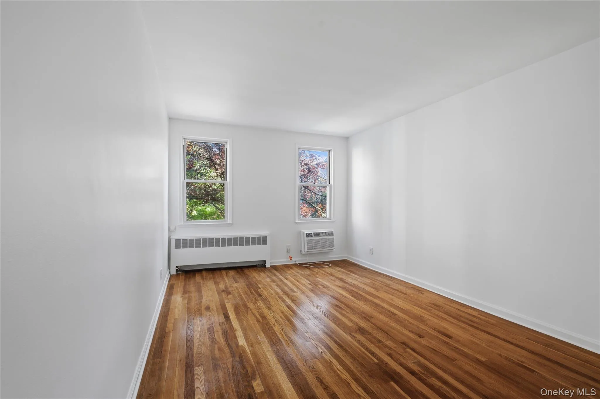 Interior room featuring wood-finish flooring, white painted walls, and white baseboards Interior room featuring wood-finish flooring, white painted walls, and white baseboards