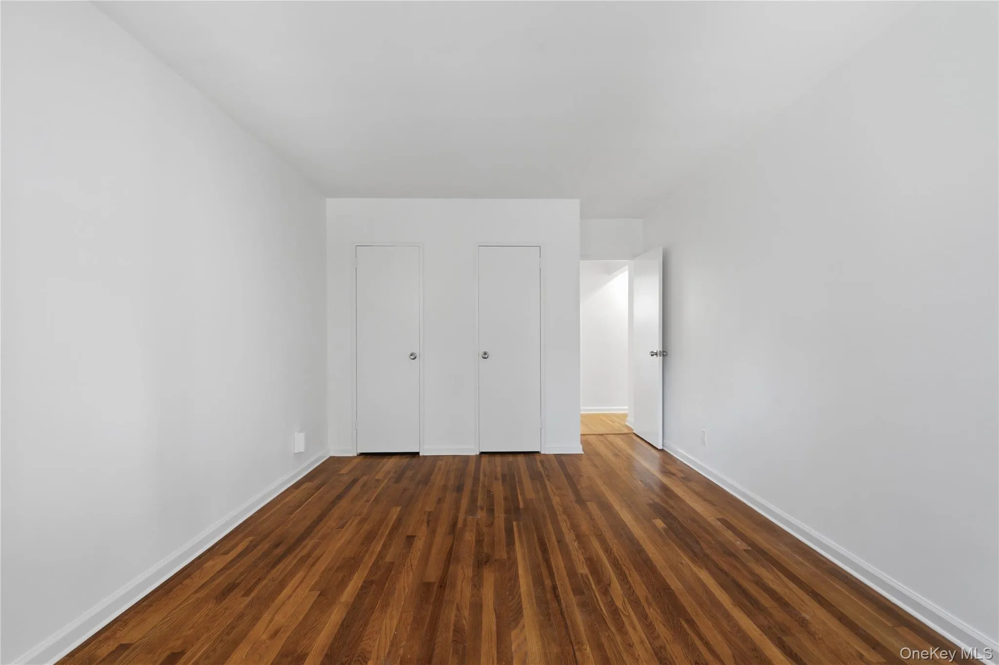 Room featuring wood-finish flooring, white walls, and bright white baseboards Room featuring wood-finish flooring, white walls, and bright white baseboards
