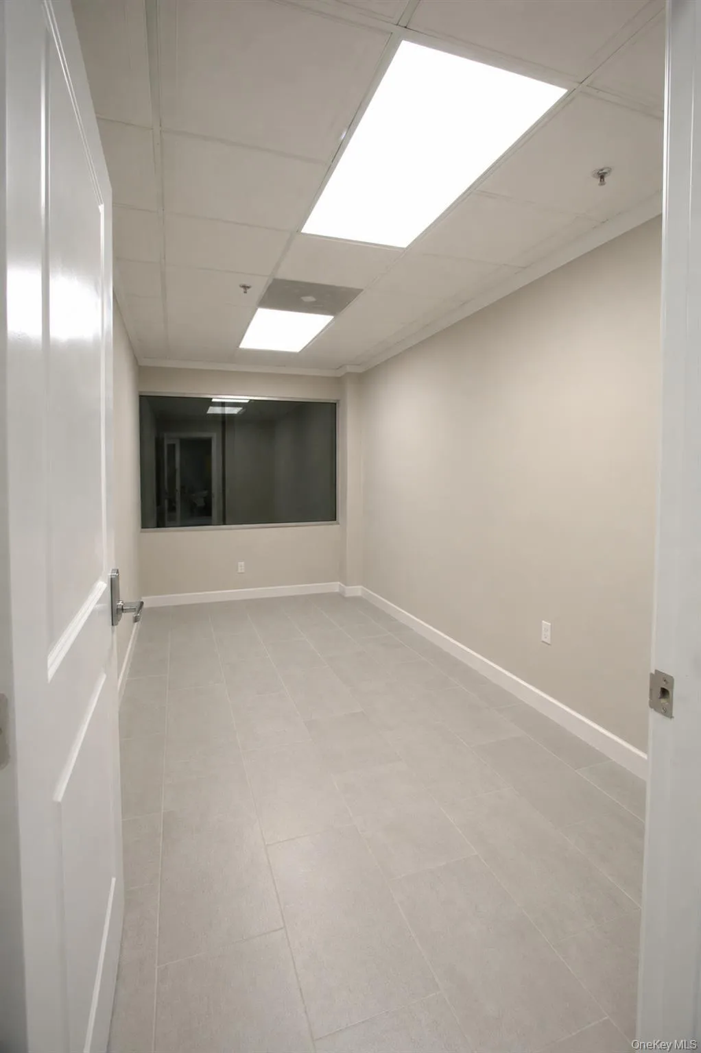 Recessed lighting, drop ceiling, light grey wall paint, large format tile flooring, and a window with a dark frame Recessed lighting, drop ceiling, light grey wall paint, large format tile flooring, and a window with a dark frame