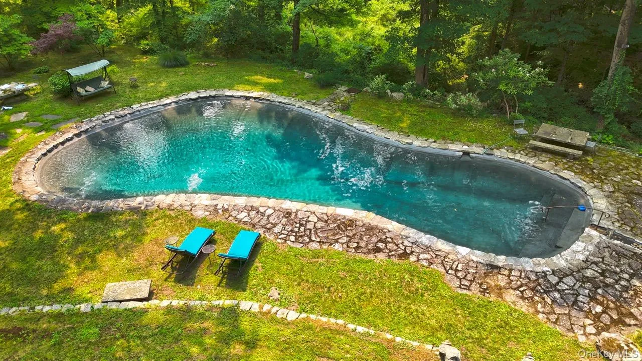 Freeform swimming pool with stone coping surrounded by lush greenery, natural stone patio, and a stone bench Freeform swimming pool with stone coping surrounded by lush greenery, natural stone patio, and a stone bench