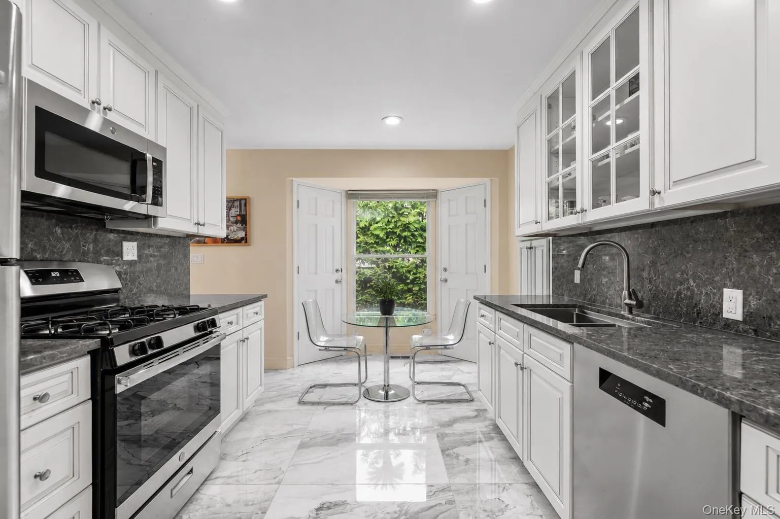 Galley kitchen featuring white cabinetry, dark stone countertops, stainless steel appliances, tile flooring Galley kitchen featuring white cabinetry, dark stone countertops, stainless steel appliances, tile flooring
