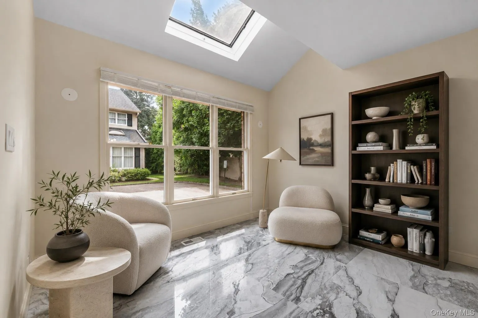 Vaulted ceiling with an integrated skylight illuminates a room featuring polished stone-finish flooring, a large multi-pane window Vaulted ceiling with an integrated skylight illuminates a room featuring polished stone-finish flooring, a large multi-pane window