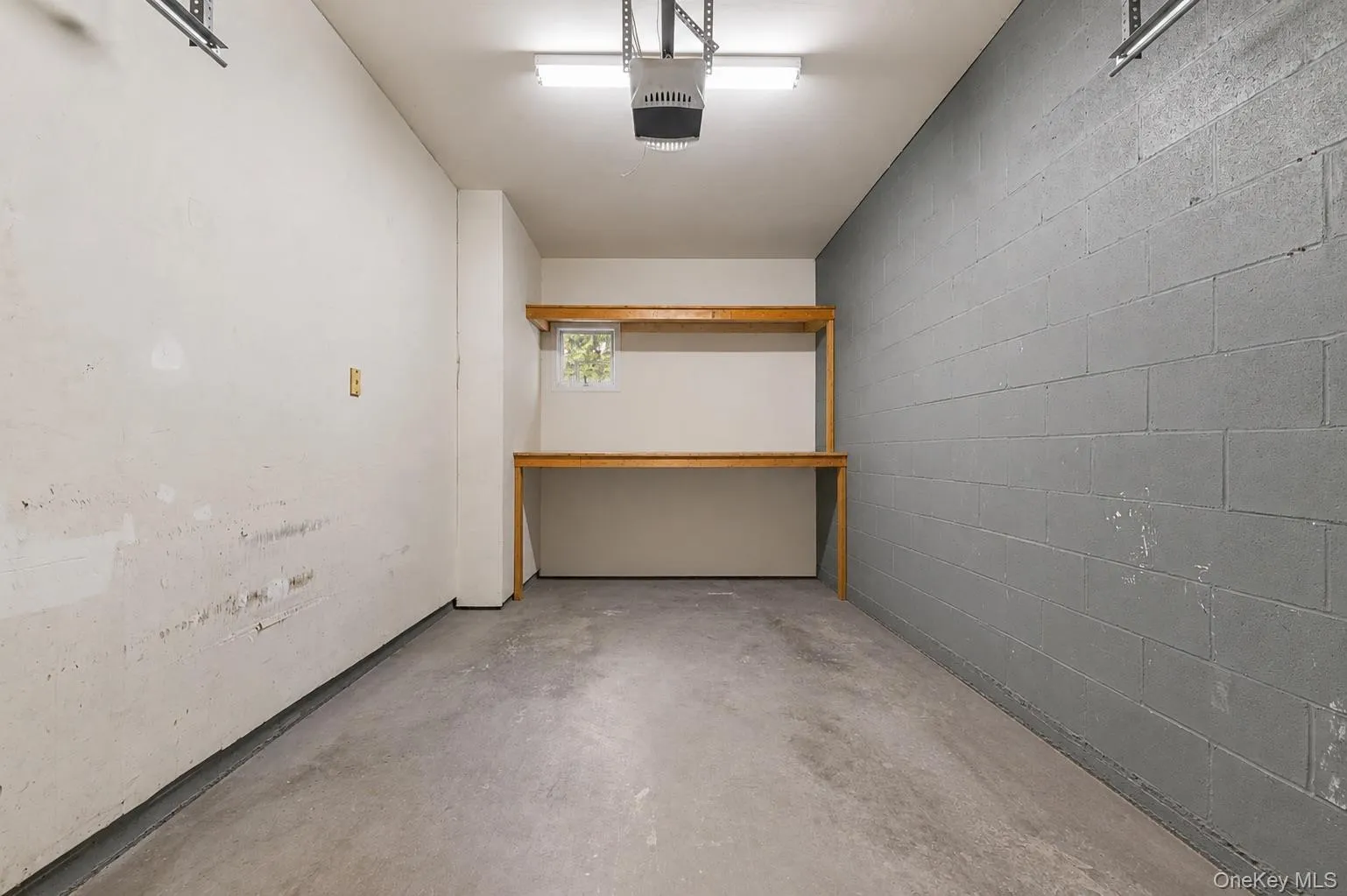 Garage interior featuring concrete flooring and a built-in wooden workbench with shelving Garage interior featuring concrete flooring and a built-in wooden workbench with shelving