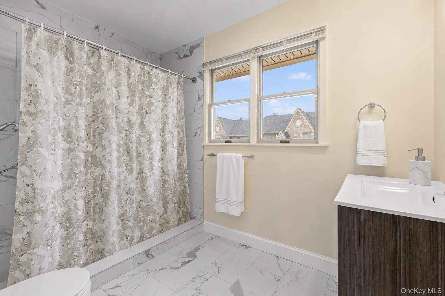 Bathroom featuring a white vanity with integrated sink, wood-finish cabinetry, and a dual-pane window Bathroom featuring a white vanity with integrated sink, wood-finish cabinetry, and a dual-pane window
