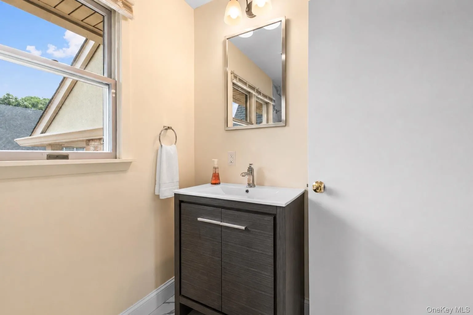 Bathroom vanity featuring a dark wood-finish cabinet with silver hardware, an integrated white sink, and a coordinating silver-framed mirror Bathroom vanity featuring a dark wood-finish cabinet with silver hardware, an integrated white sink, and a coordinating silver-framed mirror
