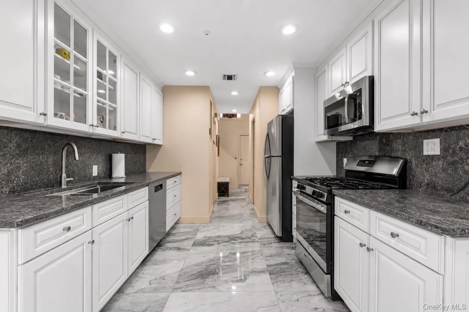 Modern kitchen featuring white shaker cabinetry, stainless steel appliances, granite countertops, a deep basin sink with a gooseneck faucet, and tile flooring Modern kitchen featuring white shaker cabinetry, stainless steel appliances, granite countertops, a deep basin sink with a gooseneck faucet, and tile flooring