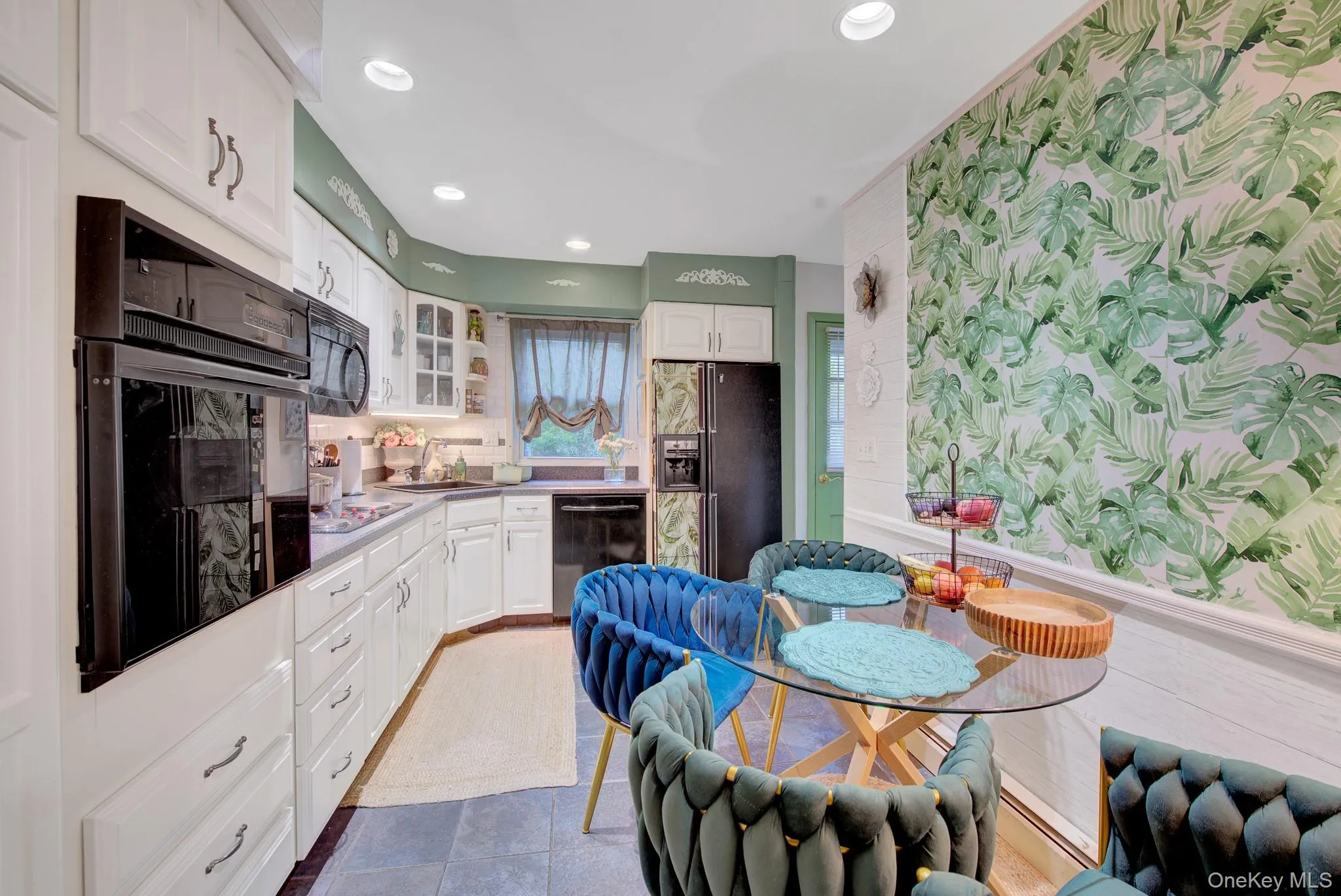 Kitchen featuring extensive white cabinetry, built-in black appliances, recessed lighting, and a dining area with a glass-top table Kitchen featuring extensive white cabinetry, built-in black appliances, recessed lighting, and a dining area with a glass-top table