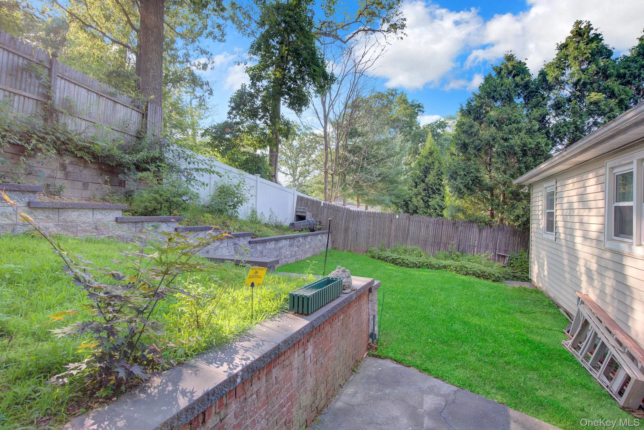 Expansive backyard featuring a lush lawn, concrete patio, and a shingled exterior wall with multiple windows Expansive backyard featuring a lush lawn, concrete patio, and a shingled exterior wall with multiple windows
