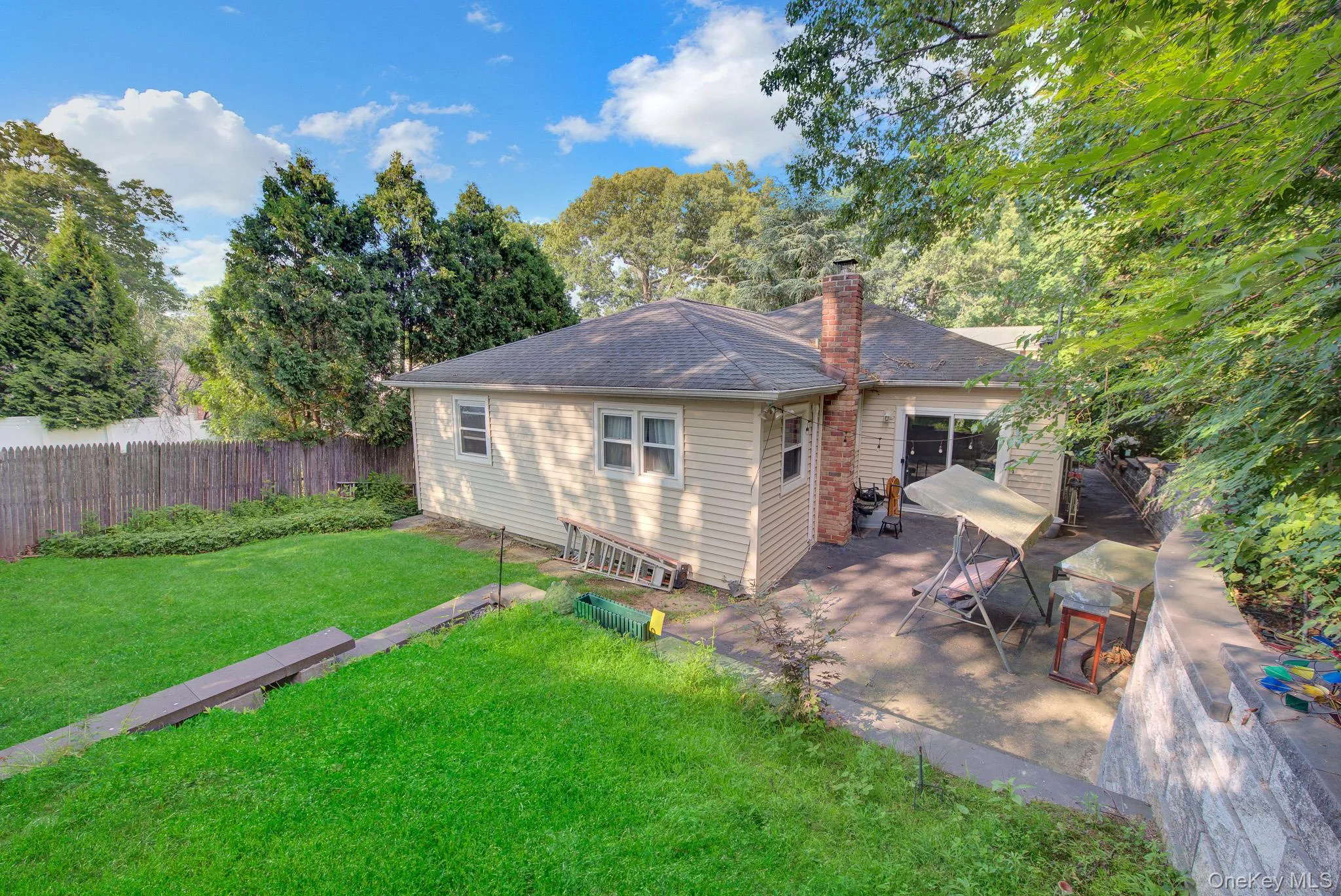 Spacious backyard featuring a lush lawn, privacy fencing, mature trees, a concrete patio, and sliding glass door access to the interior Spacious backyard featuring a lush lawn, privacy fencing, mature trees, a concrete patio, and sliding glass door access to the interior