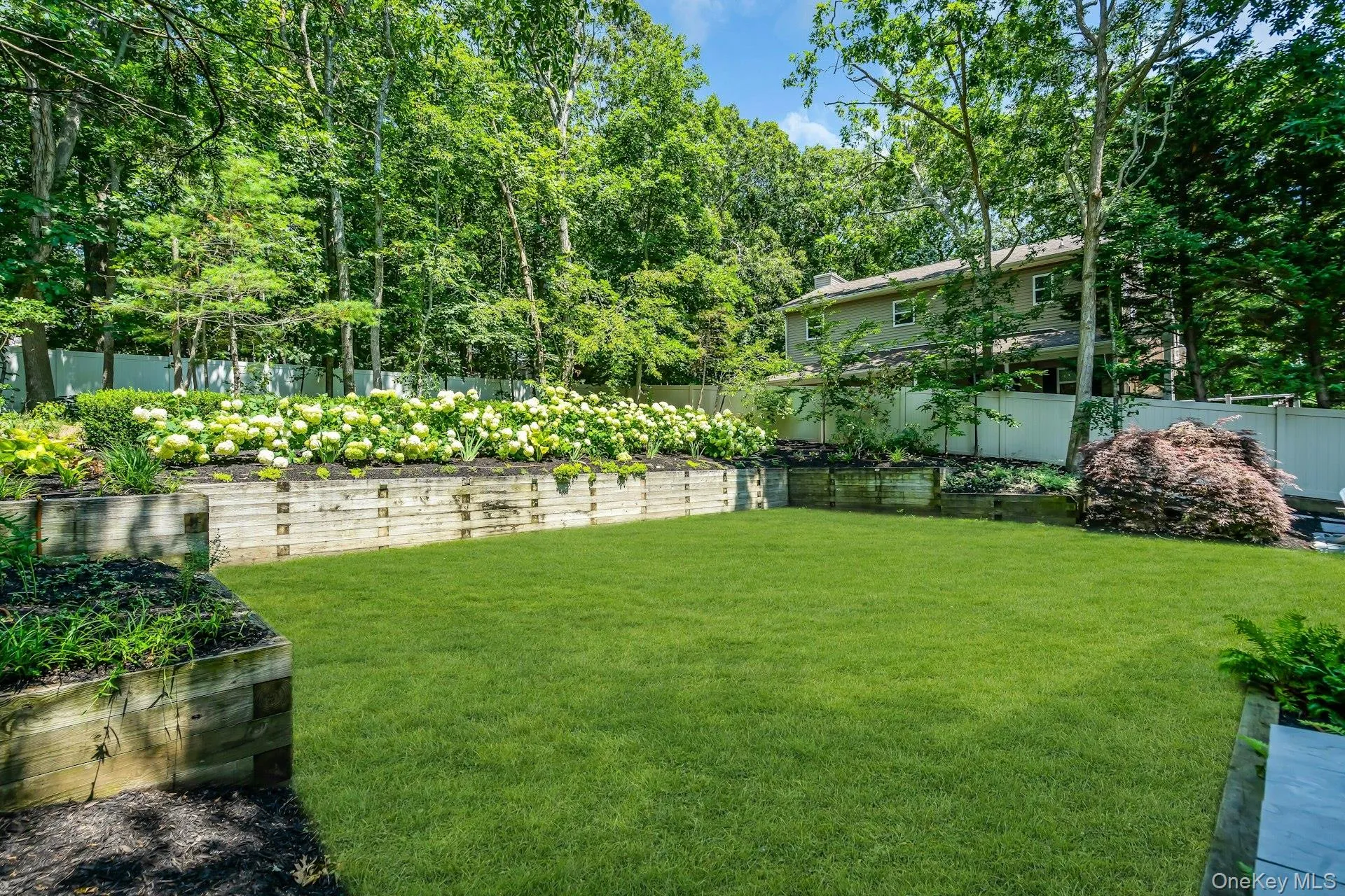 Expansive backyard featuring a lush lawn, tiered timber retaining walls, and mature flowering shrubs Expansive backyard featuring a lush lawn, tiered timber retaining walls, and mature flowering shrubs