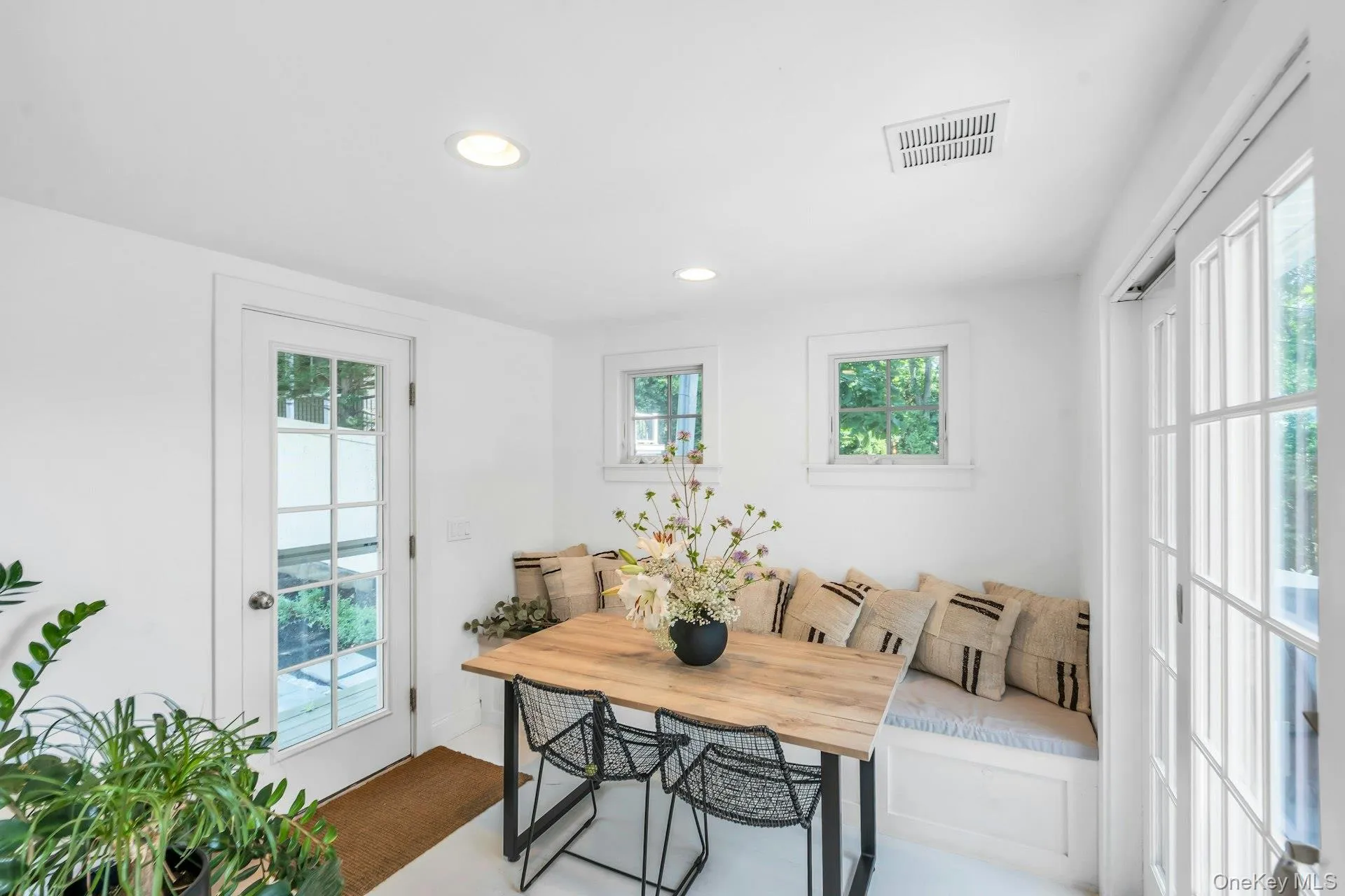 Built-in banquette seating with storage, natural wood-finish dining table, recessed lighting, and white French doors Built-in banquette seating with storage, natural wood-finish dining table, recessed lighting, and white French doors