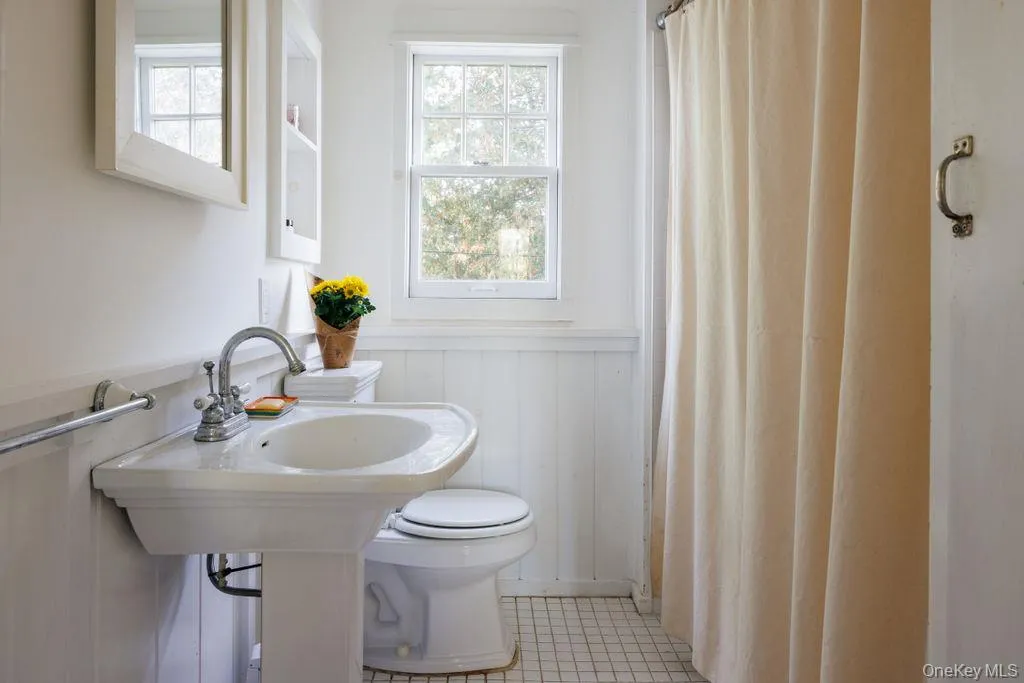Full bath featuring wainscoting, a shower with shower curtain, and tile patterned floors Full bath featuring wainscoting, a shower with shower curtain, and tile patterned floors