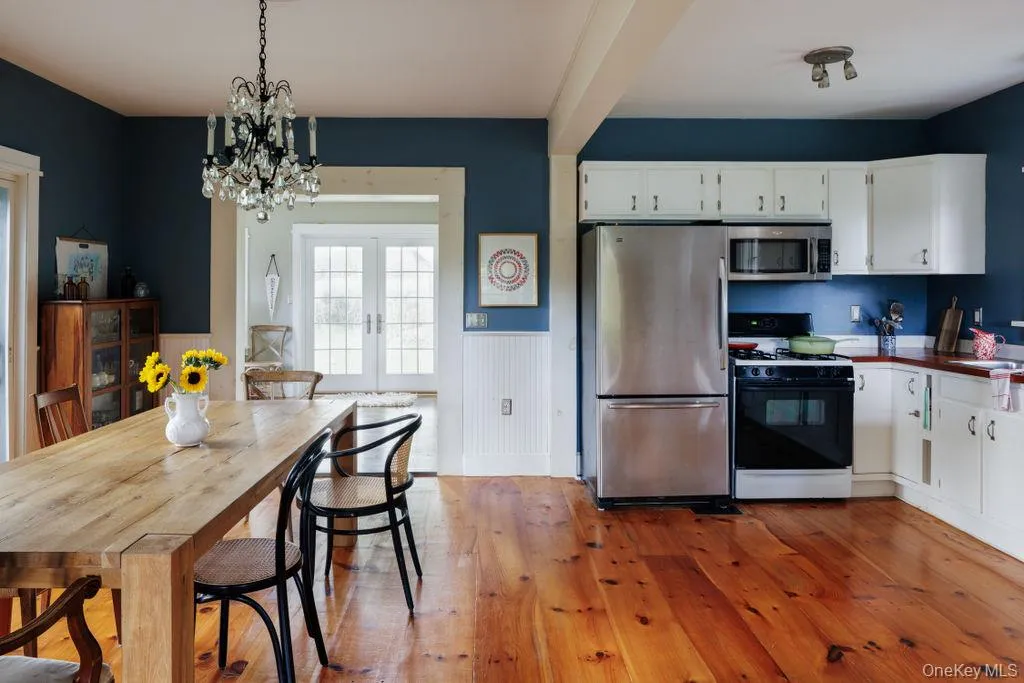 Kitchen featuring a wainscoted wall, stainless steel appliances, light wood-style flooring, a chandelier, and white cabinets Kitchen featuring a wainscoted wall, stainless steel appliances, light wood-style flooring, a chandelier, and white cabinets