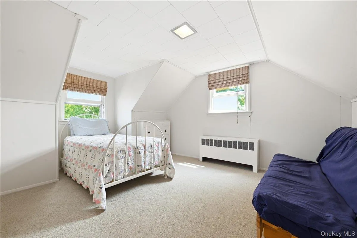 Carpeted room featuring a sloped ceiling, two windows with woven shades, a baseboard heating unit, and a recessed ceiling light fixture Carpeted room featuring a sloped ceiling, two windows with woven shades, a baseboard heating unit, and a recessed ceiling light fixture
