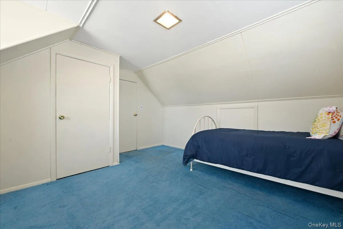 Carpeted room featuring a sloped ceiling, two paneled doors, and a flush-mount ceiling light fixture Carpeted room featuring a sloped ceiling, two paneled doors, and a flush-mount ceiling light fixture