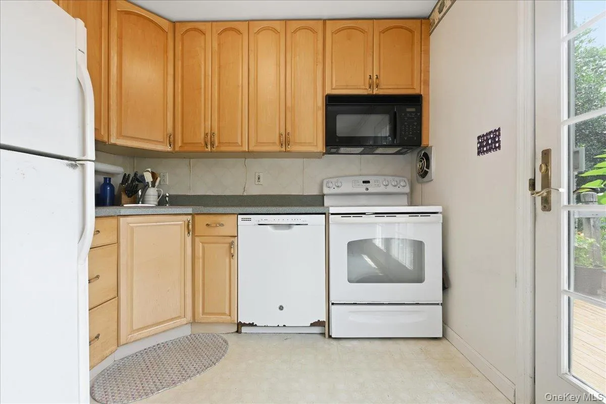 Kitchen featuring light wood-finish cabinetry, a black over-range microwave, and white appliances including a refrigerator, dishwasher, and range Kitchen featuring light wood-finish cabinetry, a black over-range microwave, and white appliances including a refrigerator, dishwasher, and range