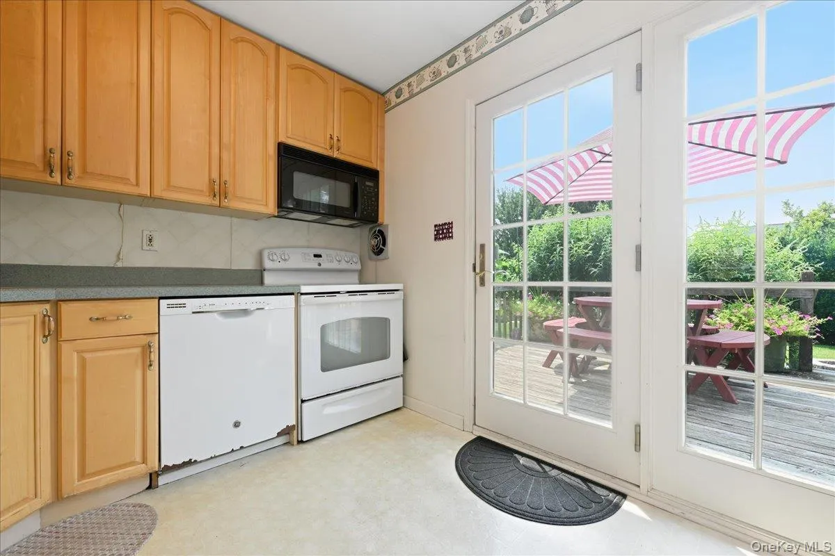 Kitchen with light wood cabinetry, white appliances, and a dark countertop Kitchen with light wood cabinetry, white appliances, and a dark countertop