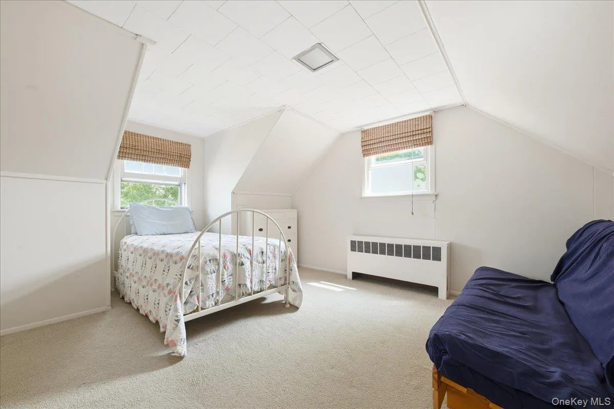 Carpeted room featuring an attic ceiling design, two windows with woven shades, a built-in radiator, and recessed lighting Carpeted room featuring an attic ceiling design, two windows with woven shades, a built-in radiator, and recessed lighting