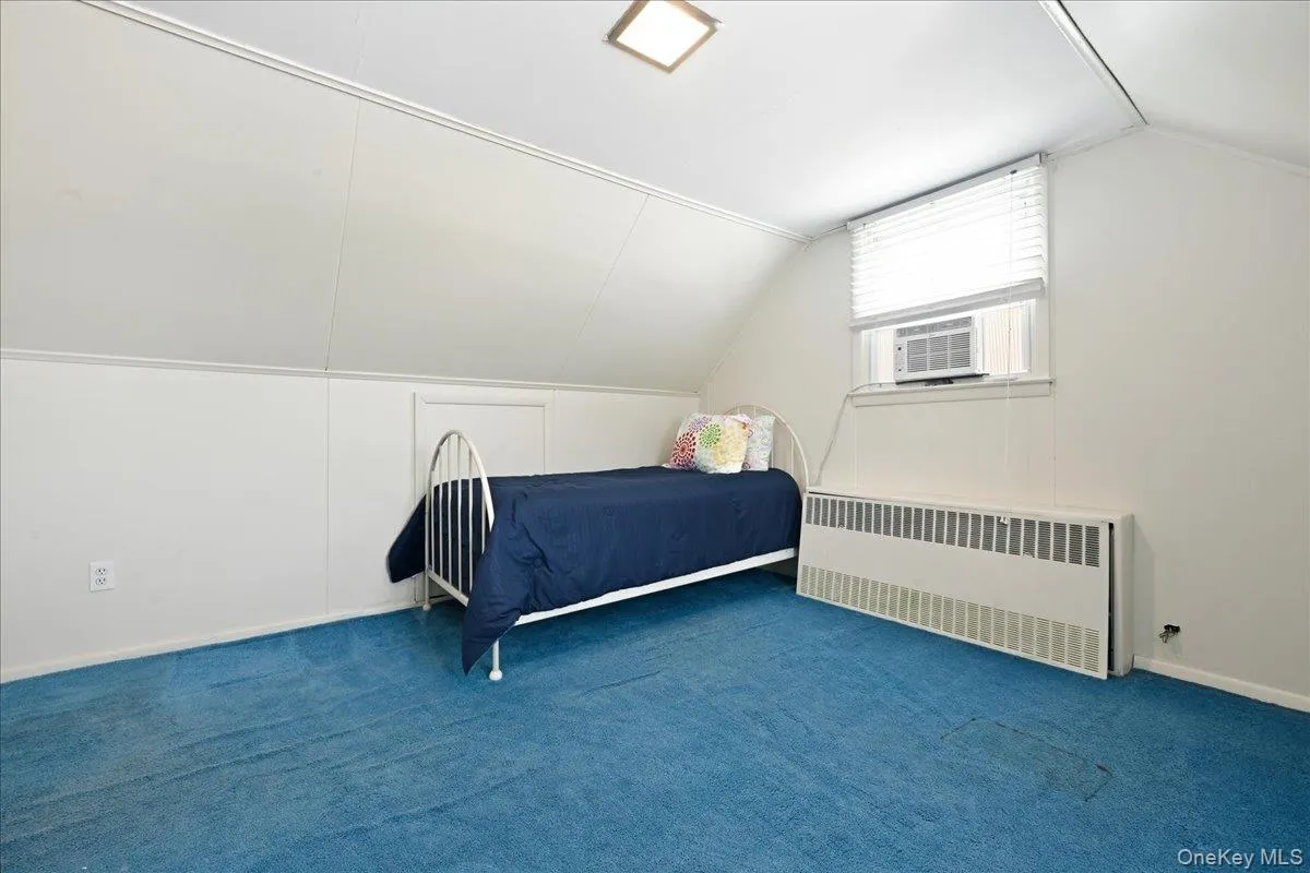 Room featuring blue carpeting, white wall paneling, and an angled ceiling line Room featuring blue carpeting, white wall paneling, and an angled ceiling line