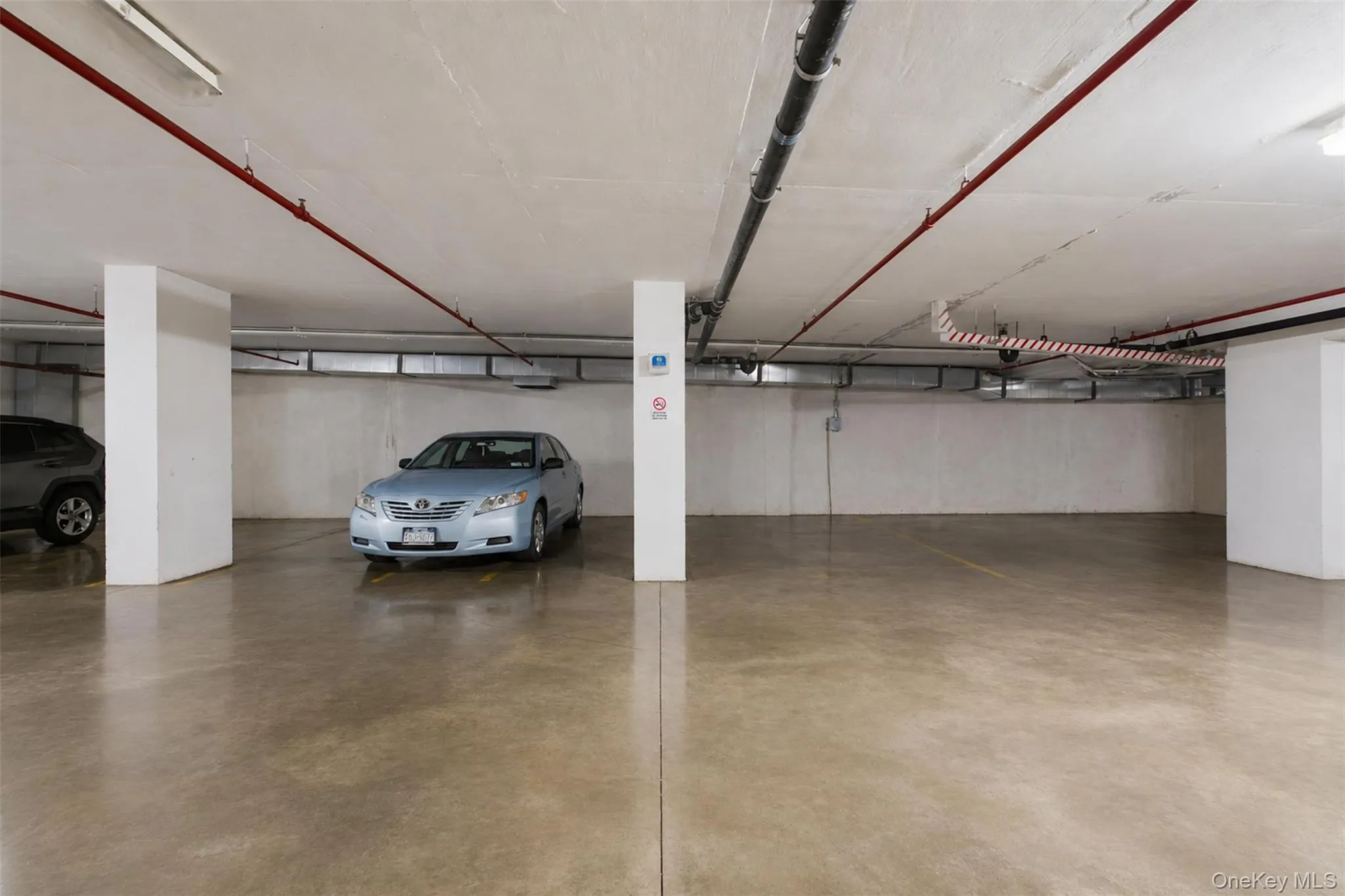 2 Dedicated parking spaces within a subterranean garage, featuring polished concrete flooring and overhead utility lines 2 Dedicated parking spaces within a subterranean garage, featuring polished concrete flooring and overhead utility lines