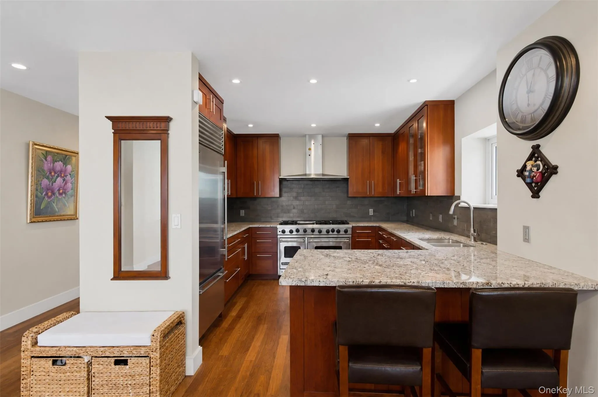Kitchen featuring wood-finish flooring, custom wood cabinetry, stainless steel appliances, and stone countertops Kitchen featuring wood-finish flooring, custom wood cabinetry, stainless steel appliances, and stone countertops