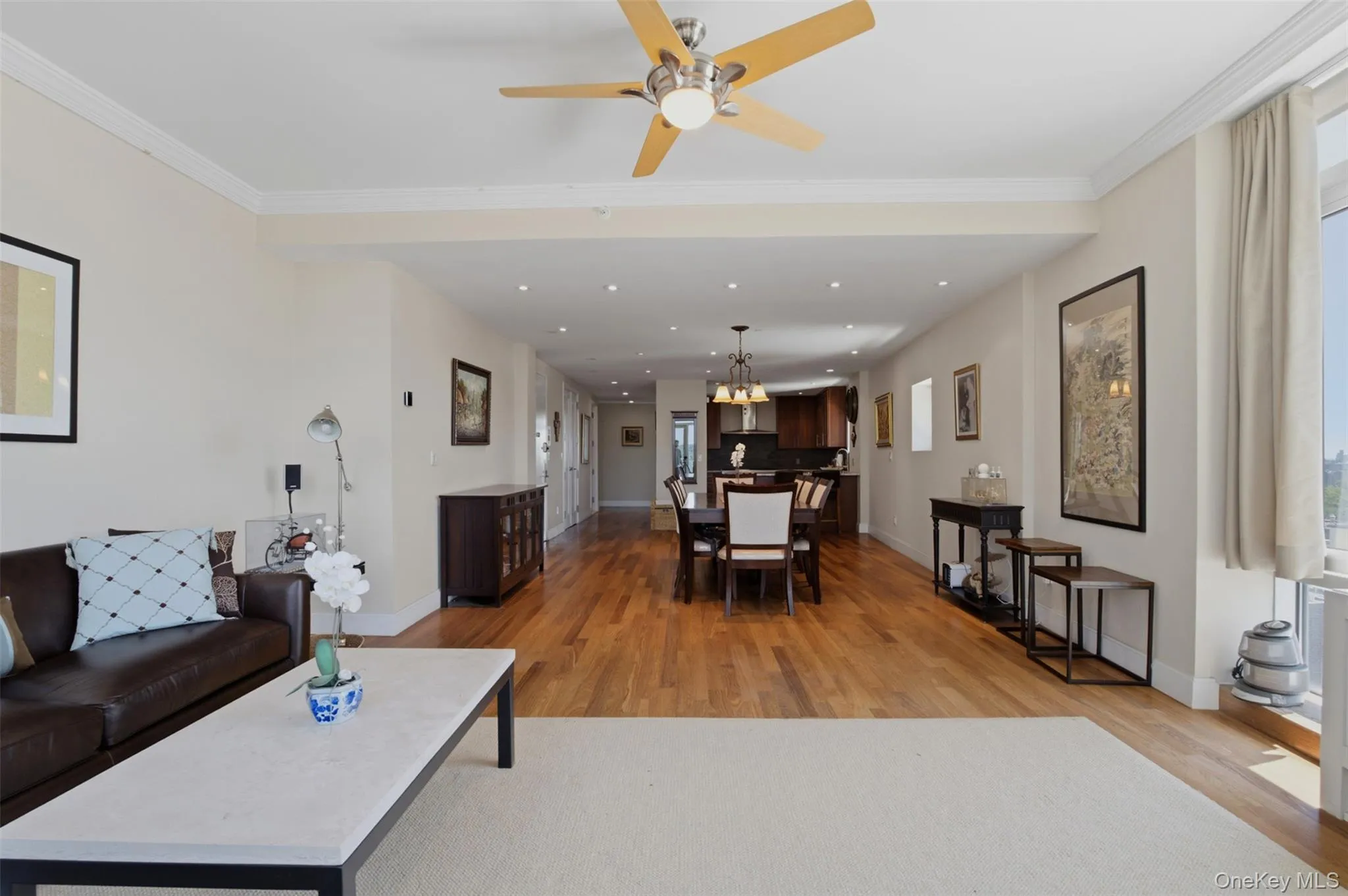 Expansive open-concept living area featuring wood-finish flooring, a ceiling fan, recessed lighting, and crown molding Expansive open-concept living area featuring wood-finish flooring, a ceiling fan, recessed lighting, and crown molding