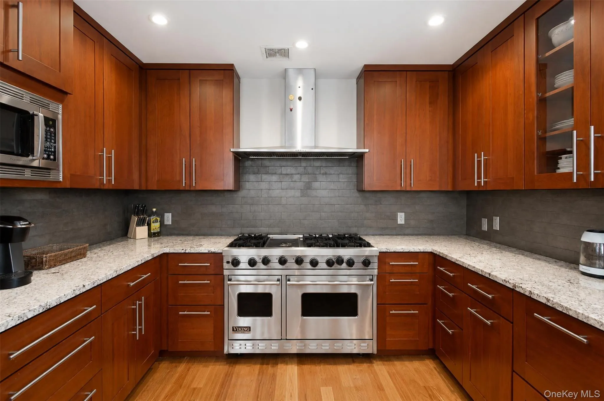 Gourmet kitchen featuring a stainless steel gas range, wood-finish cabinetry, light-toned countertops, tile backsplash, and recessed lighting Gourmet kitchen featuring a stainless steel gas range, wood-finish cabinetry, light-toned countertops, tile backsplash, and recessed lighting
