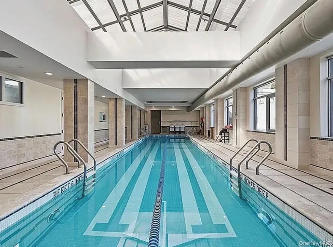 Indoor lap pool with a vaulted glass ceiling, tiled walls, and multiple windows Indoor lap pool with a vaulted glass ceiling, tiled walls, and multiple windows