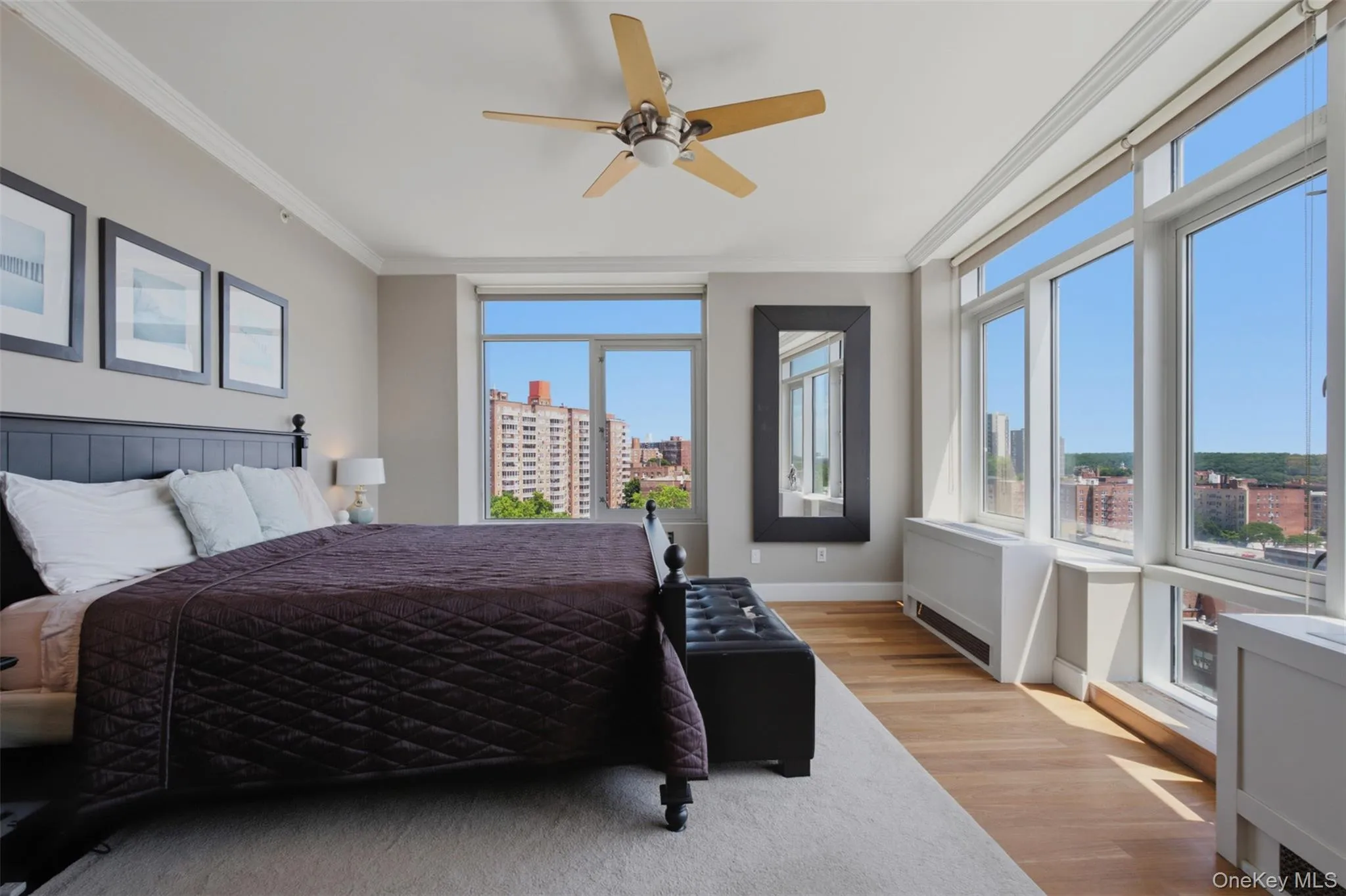 Spacious primary bedroom featuring extensive window-lines, light wood-finish flooring, and a ceiling fan Spacious primary bedroom featuring extensive window-lines, light wood-finish flooring, and a ceiling fan