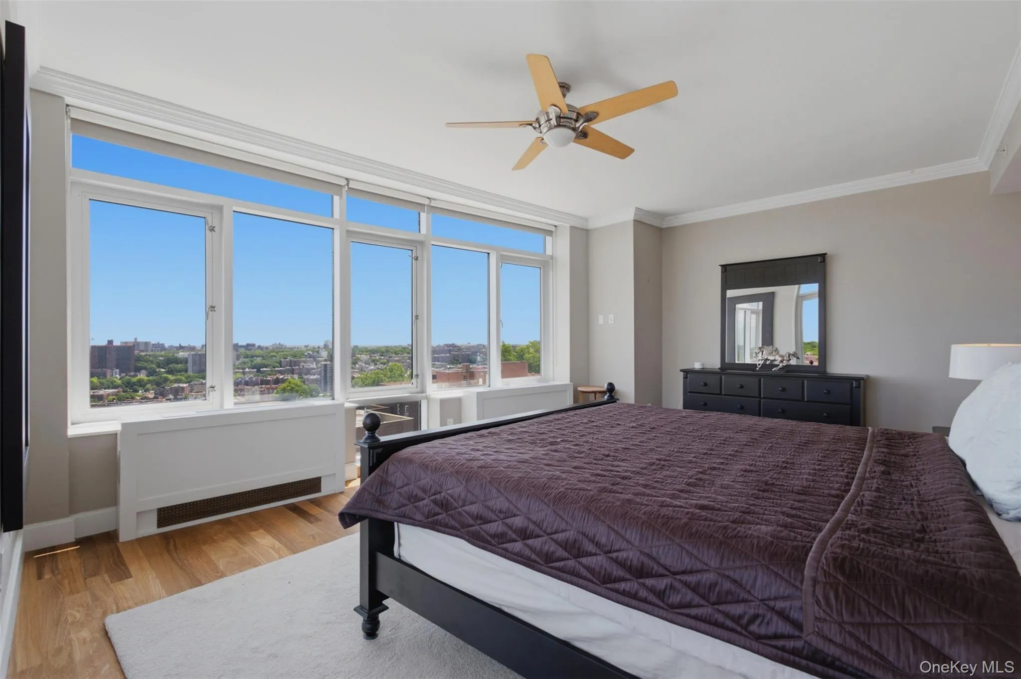 Primary bedroom featuring extensive window line, wood-finish flooring, and crown molding Primary bedroom featuring extensive window line, wood-finish flooring, and crown molding
