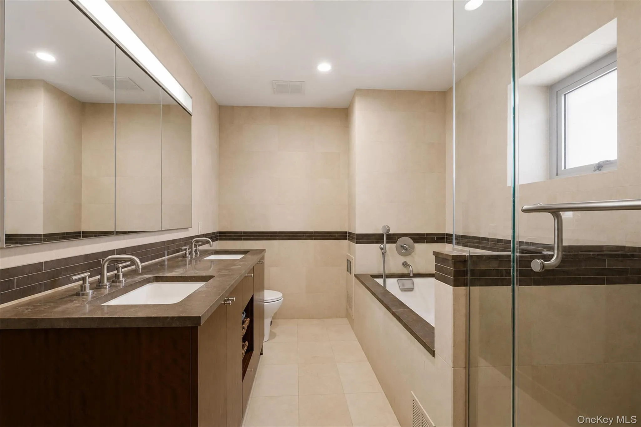 Bathroom featuring a dual vanity with integrated sinks, a built-in soaking tub, and a separate glass-enclosed shower Bathroom featuring a dual vanity with integrated sinks, a built-in soaking tub, and a separate glass-enclosed shower