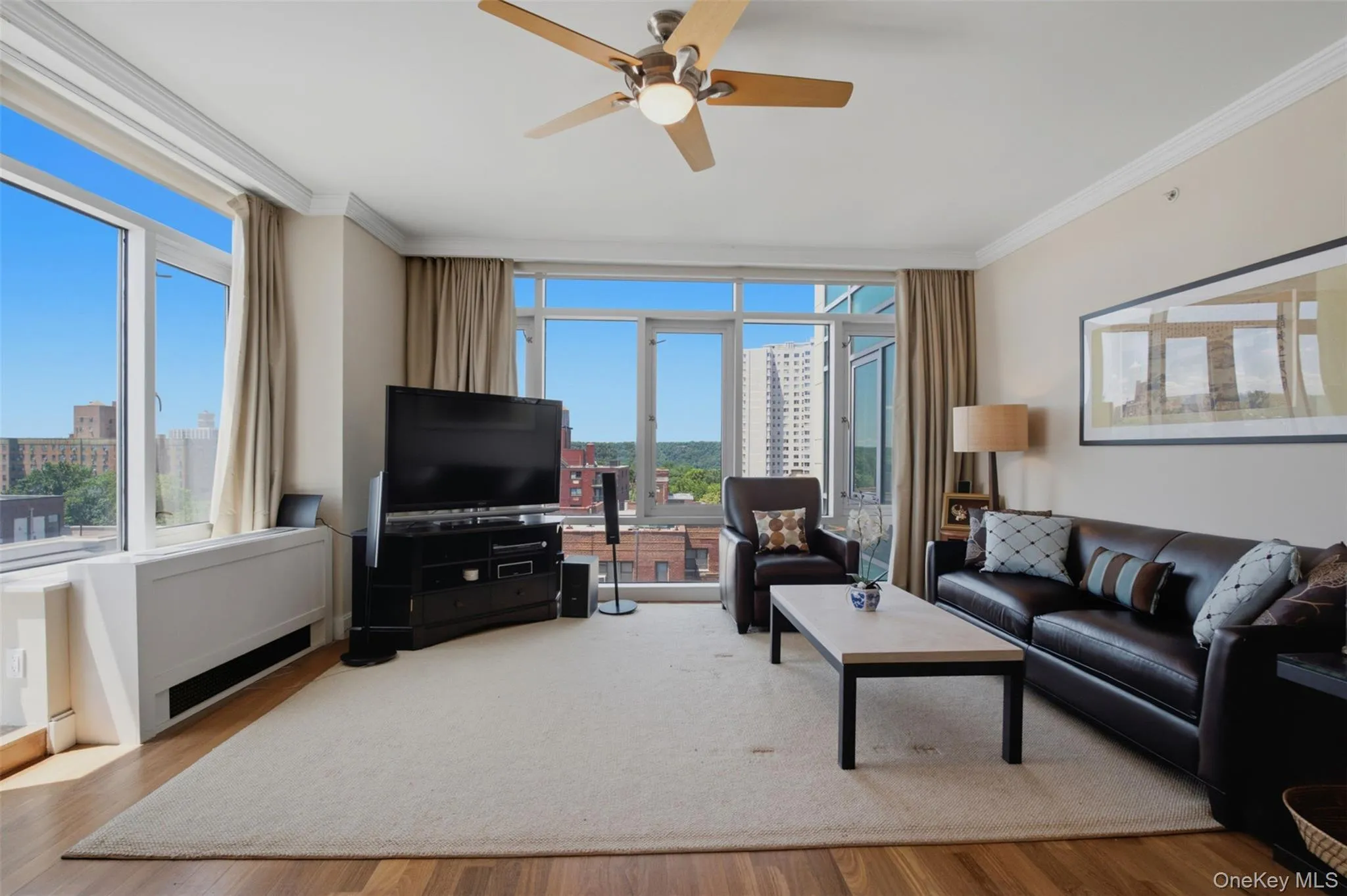 Spacious living area featuring expansive floor-to-ceiling windows, wood-finish flooring, and crown molding Spacious living area featuring expansive floor-to-ceiling windows, wood-finish flooring, and crown molding