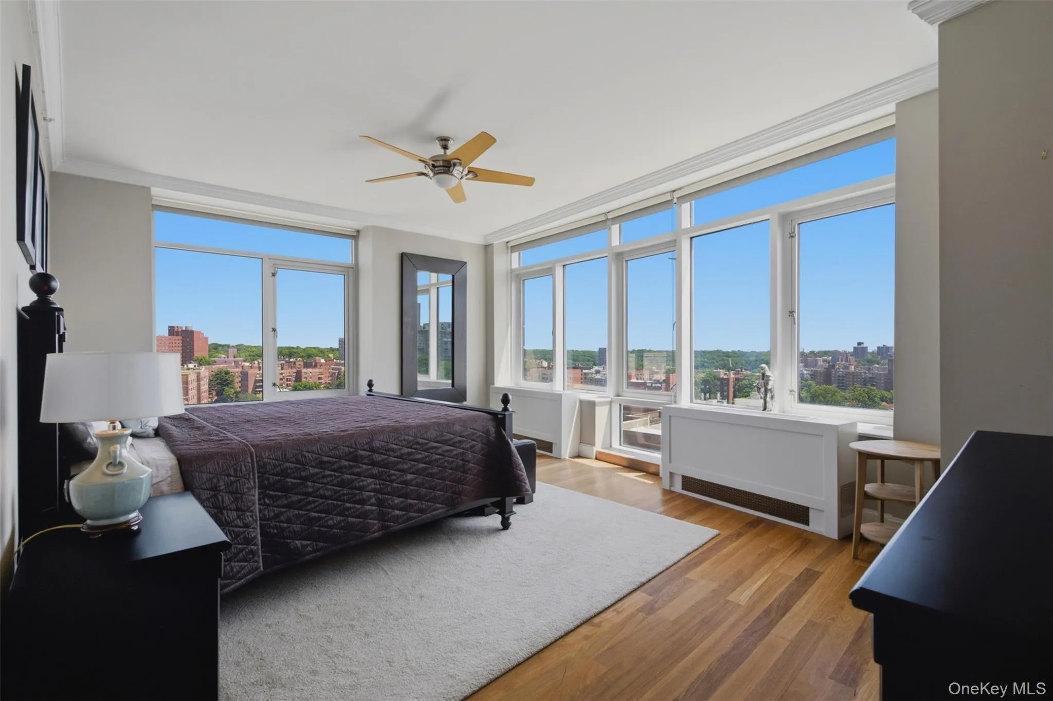Primary bedroom with expansive window wall with cityscape and green space panorama Primary bedroom with expansive window wall with cityscape and green space panorama