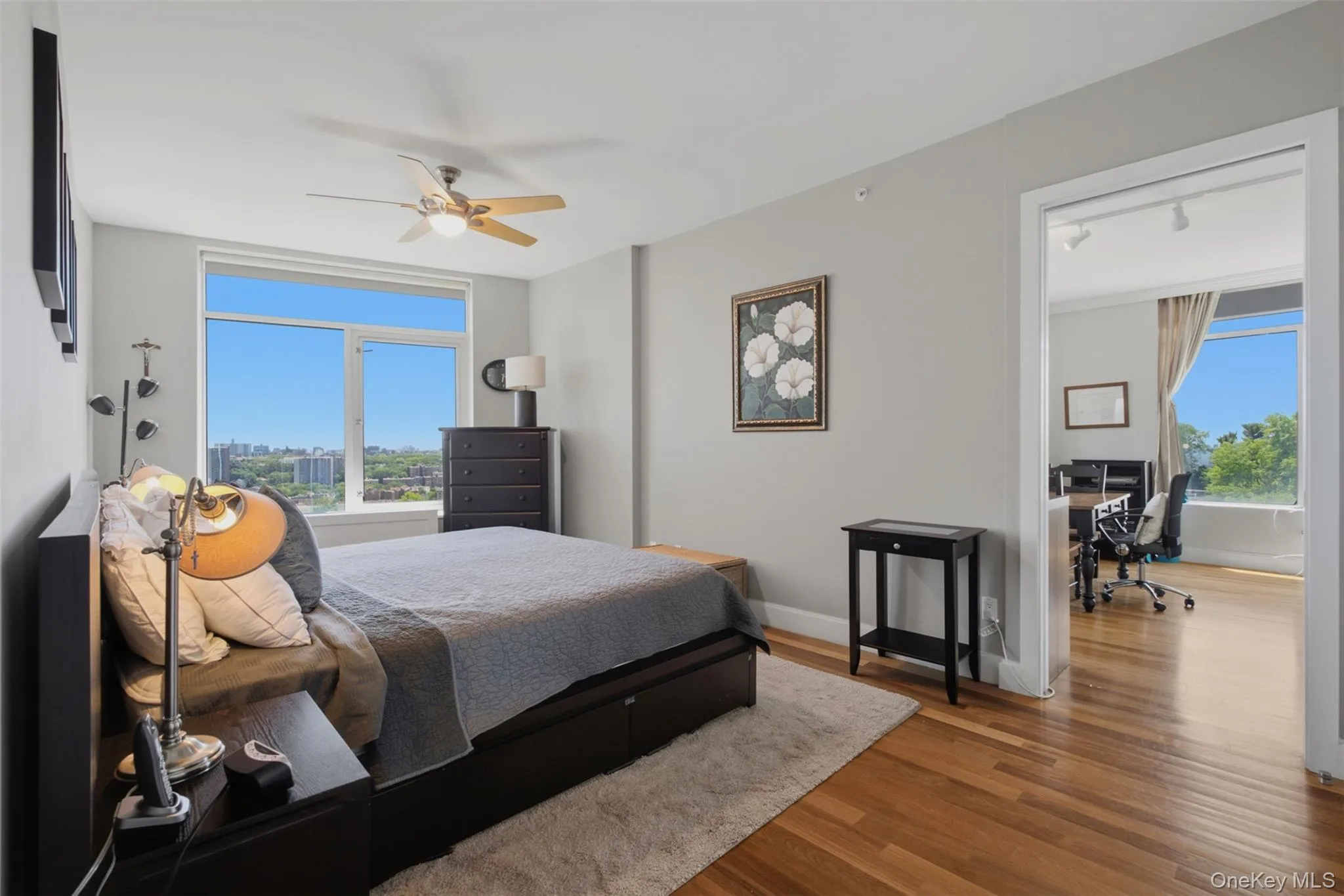 Bedroom 2 featuring a large window with city and tree-lined panoramas, wood-finish flooring, light gray wall paint, and a ceiling fan Bedroom 2 featuring a large window with city and tree-lined panoramas, wood-finish flooring, light gray wall paint, and a ceiling fan
