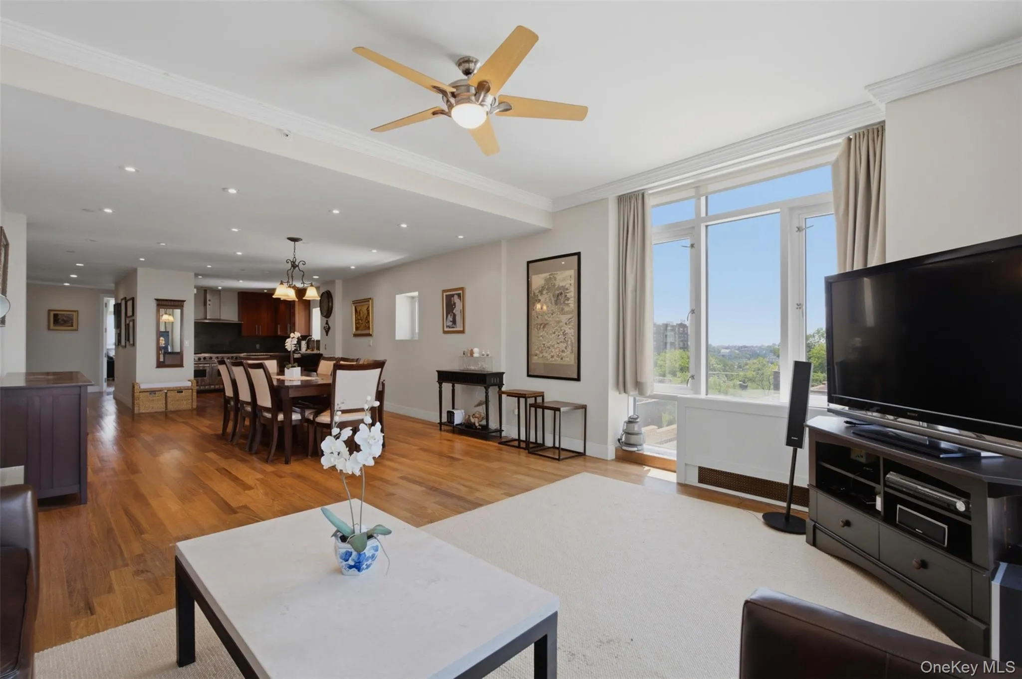 Open-concept living area with abundant natural light, crown molding, and wood-finish flooring Open-concept living area with abundant natural light, crown molding, and wood-finish flooring